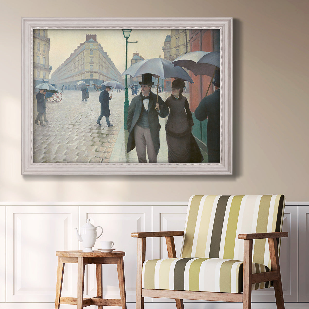 Impressionist urban street scene in the rain by Gustave Caillebotte in an ornate weathered white frame displayed in a light-toned interior setting.