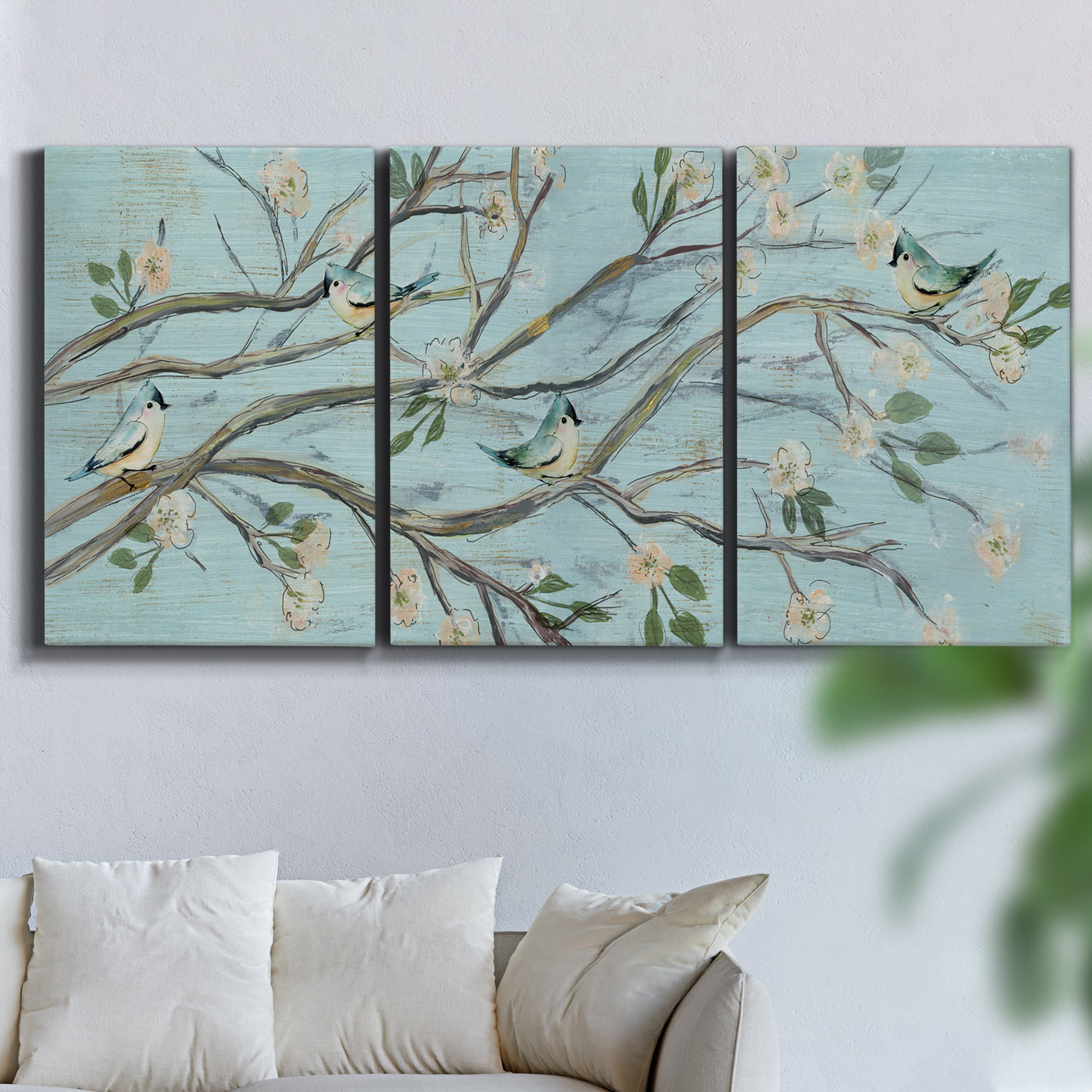 Three-panel canvas wall art featuring blue sky with flowering branches, displayed in a living room above a sofa.
