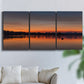 Three-panel canvas wall art featuring glowing sunset over water, displayed in a living room above a sofa.