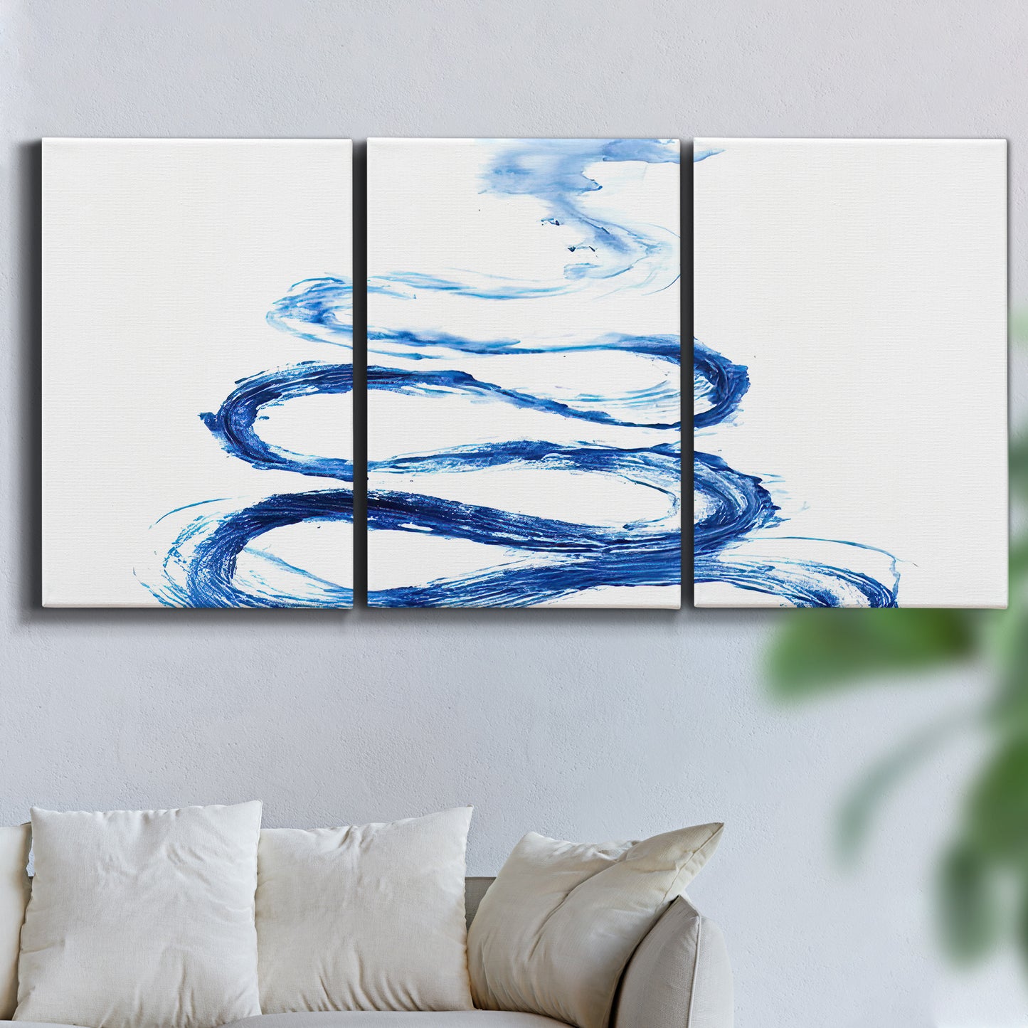 Three-panel canvas wall art featuring indigo abstract vapor watercolor, displayed in a living room above a sofa.
