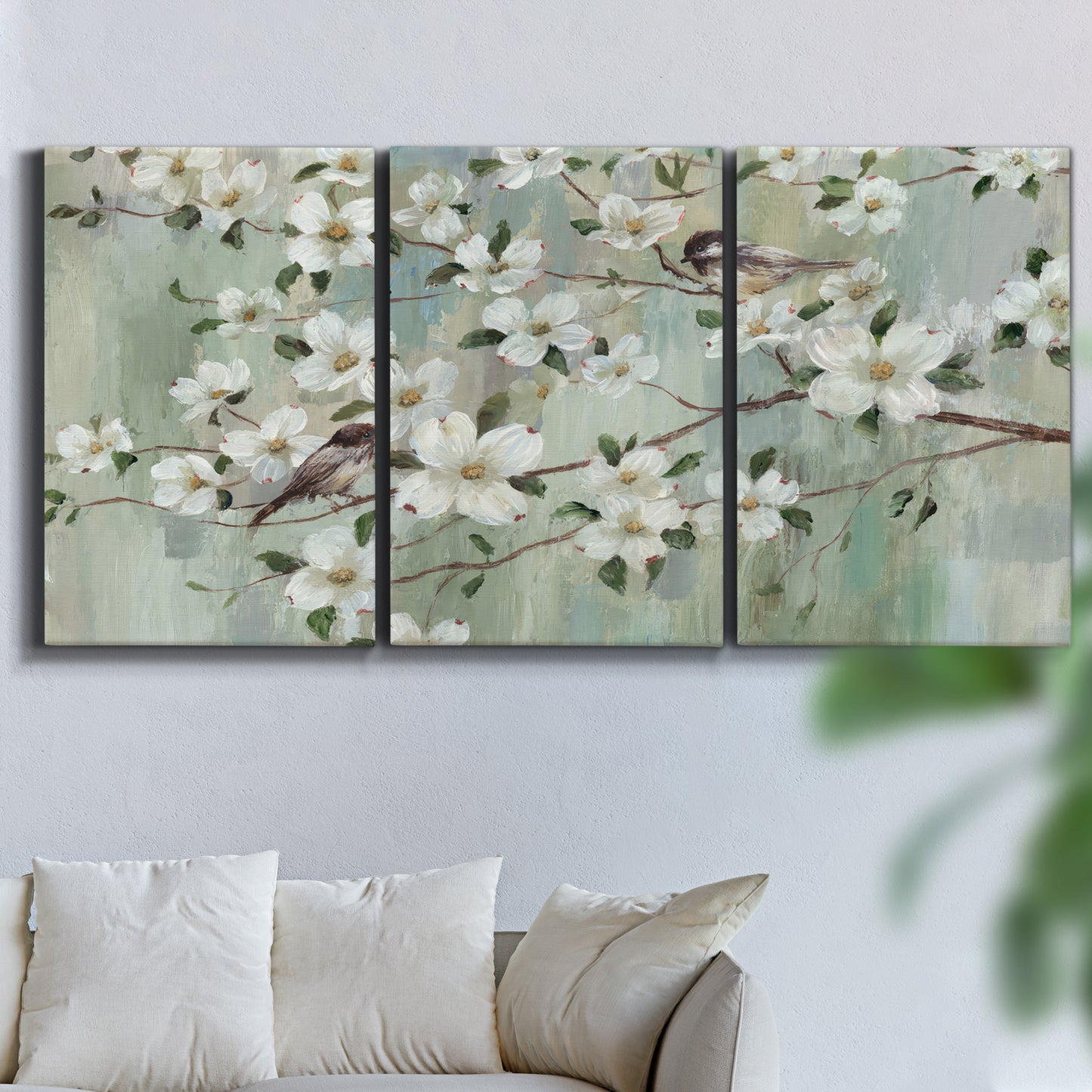 Three-panel canvas wall art featuring delicate spring blossoms with birds, displayed in a living room above a sofa.