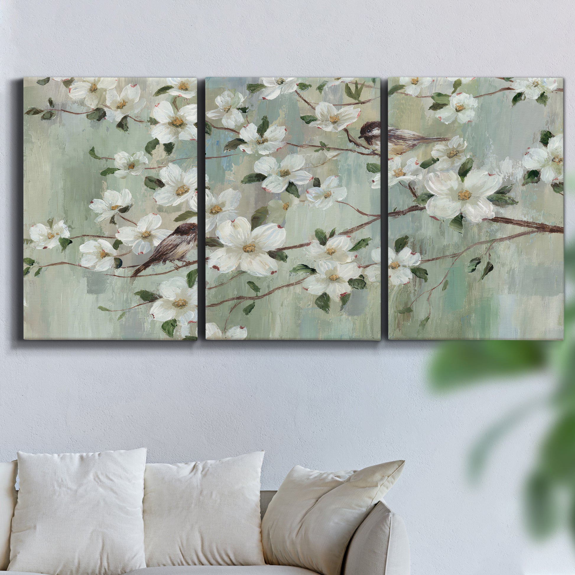 Three-panel canvas wall art featuring delicate spring blossoms with birds, displayed in a living room above a sofa.