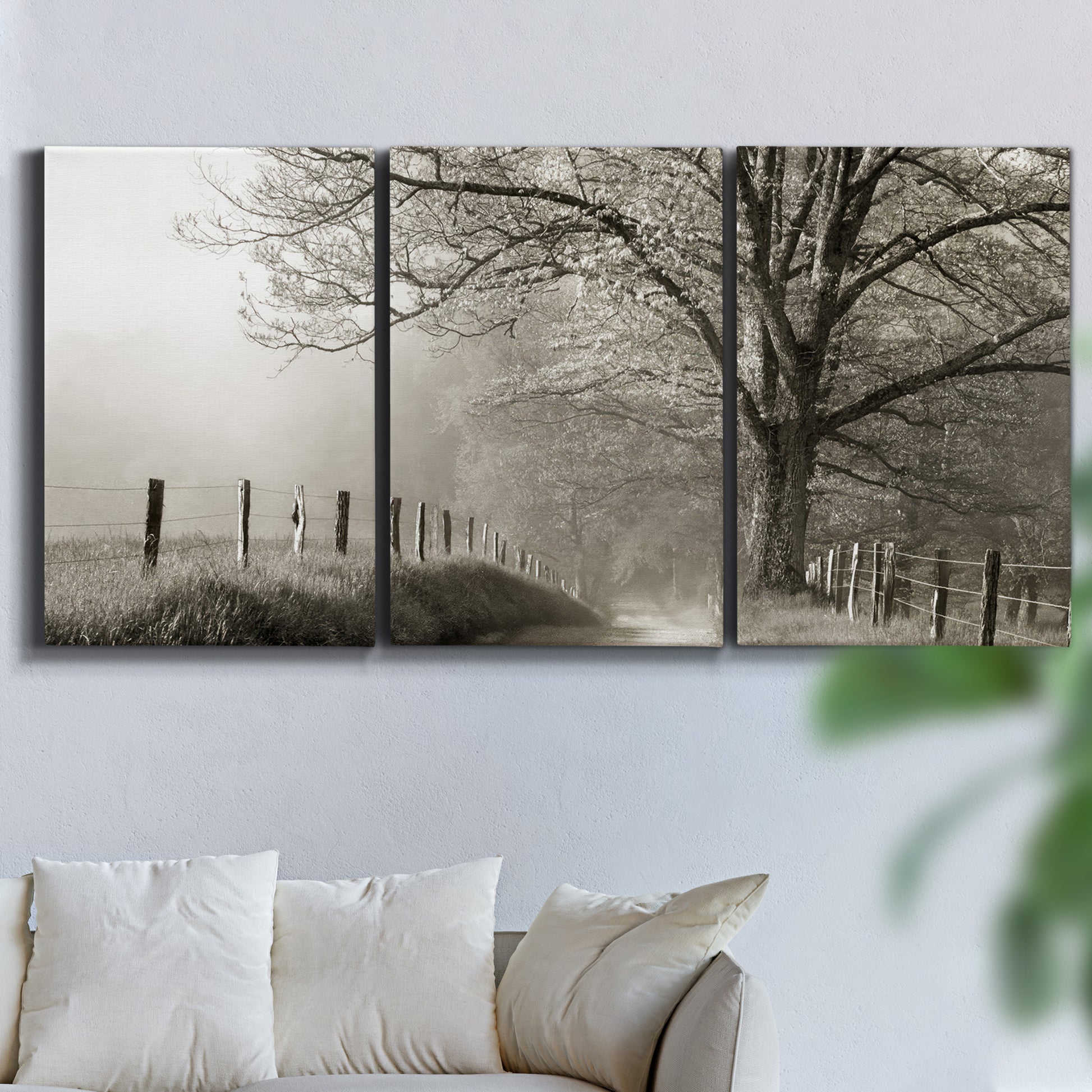Three-panel canvas wall art featuring fenced rural path through countryside, displayed in a living room above a sofa.
