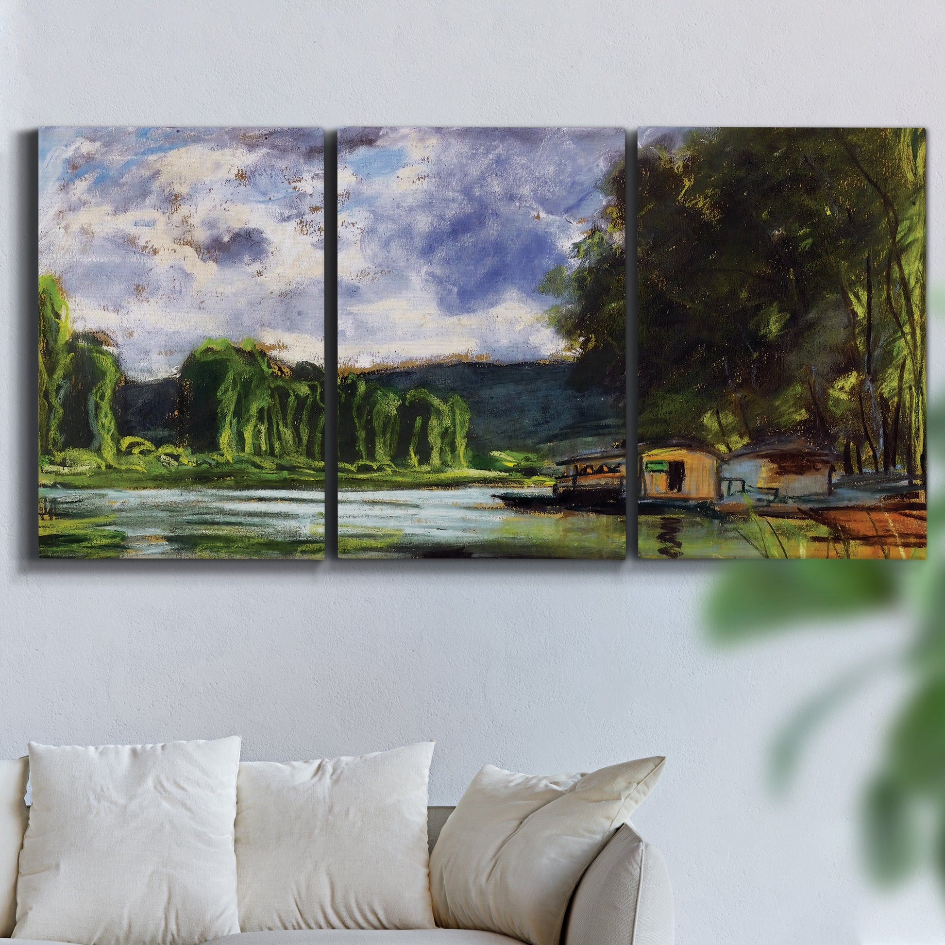 Three-panel canvas wall art featuring riverbank landscape near village, displayed in a living room above a sofa.