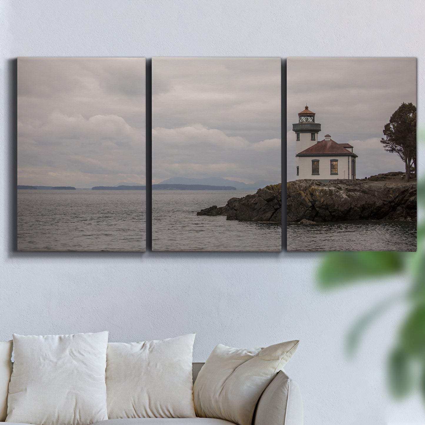 Three-panel canvas wall art featuring lighthouse watching over coastline, displayed in a living room above a sofa.