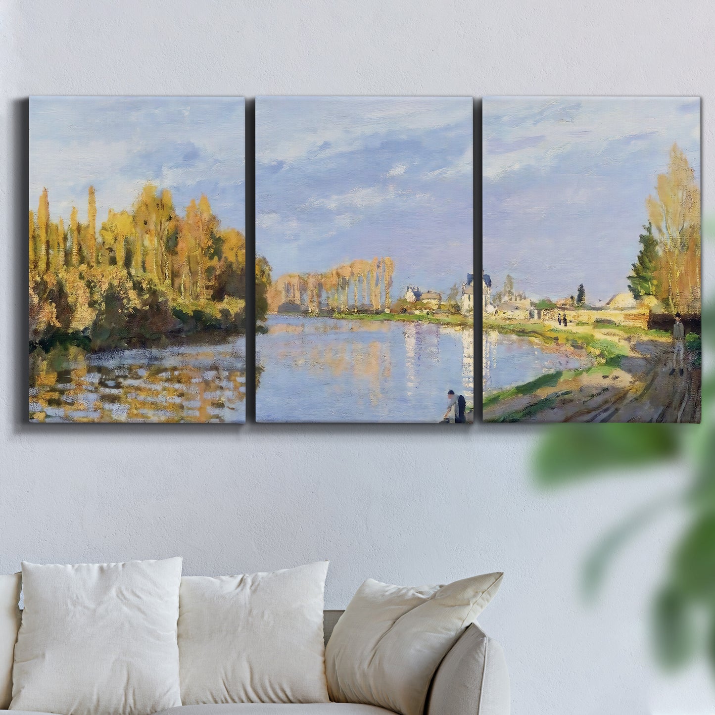 Three-panel canvas wall art featuring river flowing past village, displayed in a living room above a sofa.