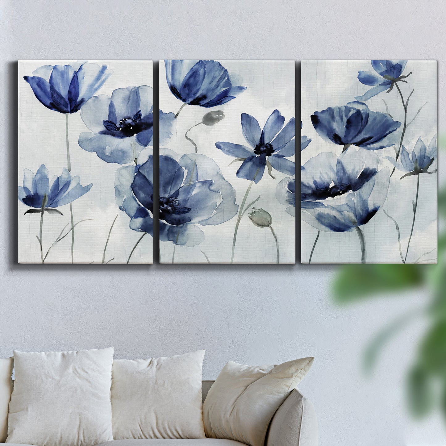 Three-panel canvas wall art featuring indigo floral blossoms awakening, displayed in a living room above a sofa.