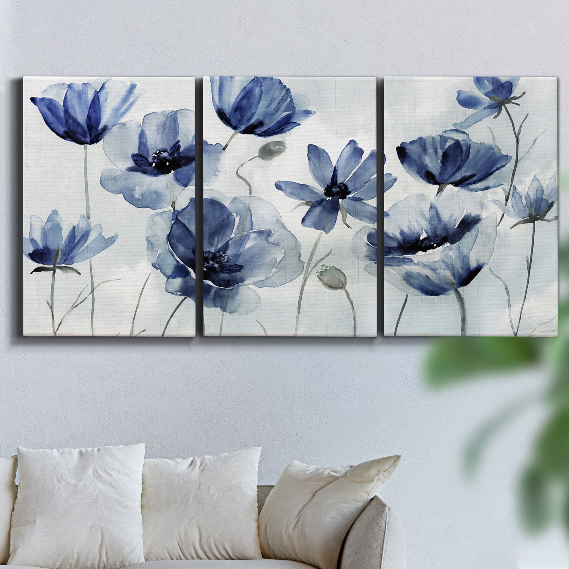 Three-panel canvas wall art featuring indigo floral blossoms awakening, displayed in a living room above a sofa.