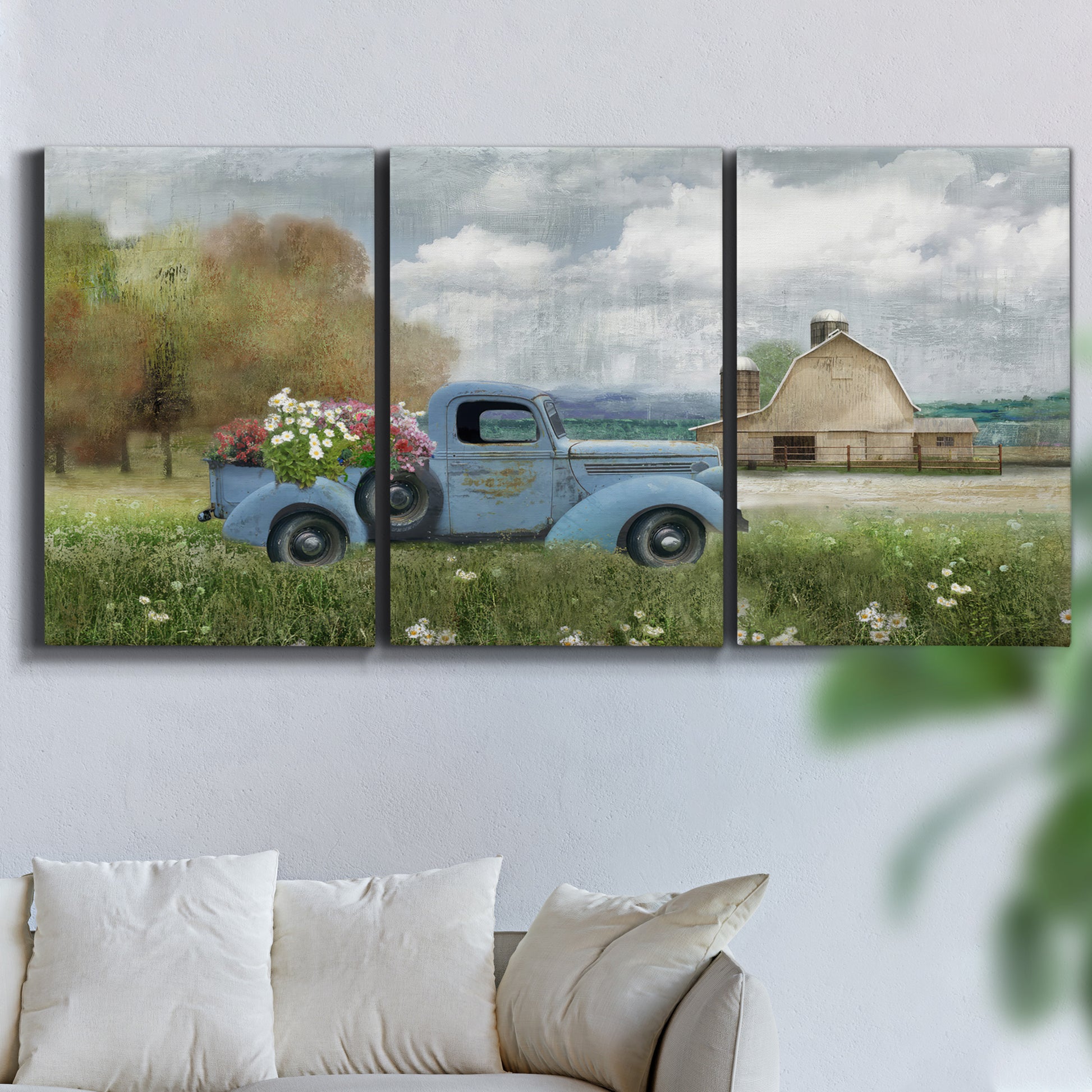 Three-panel canvas wall art featuring vintage blue truck with flower load, displayed in a living room above a sofa.