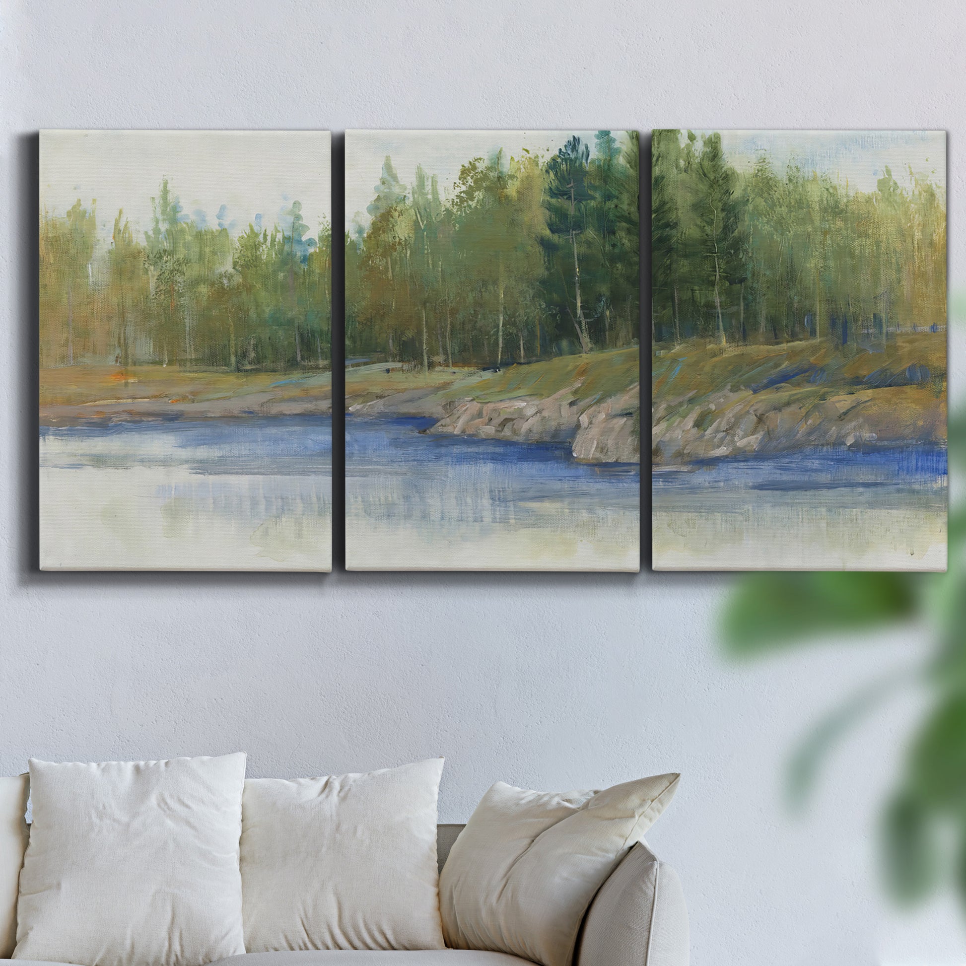 Three-panel canvas wall art featuring riverbank landscape with trees, displayed in a living room above a sofa.