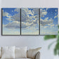 Three-panel canvas wall art featuring whimsical cloud filled sky landscape, displayed in a living room above a sofa.