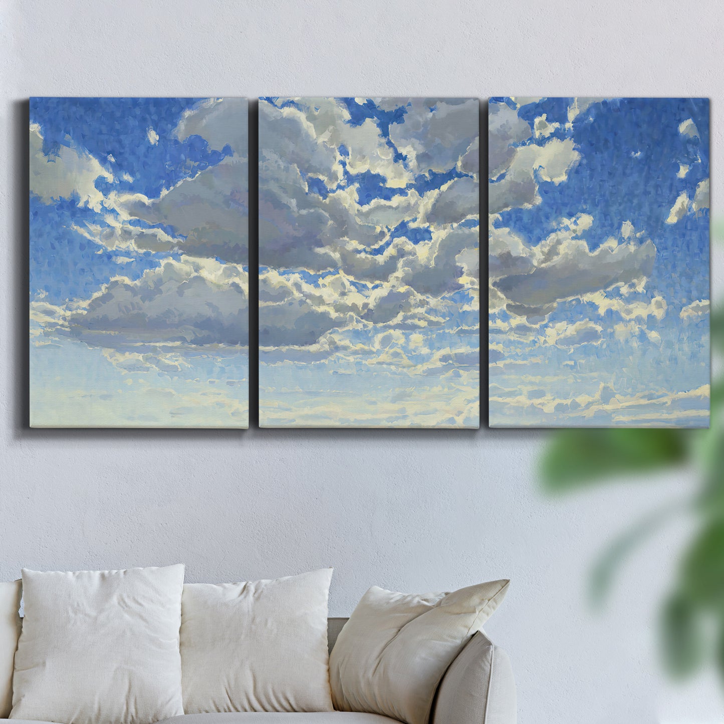 Three-panel canvas wall art featuring whimsical cloud filled sky landscape, displayed in a living room above a sofa.