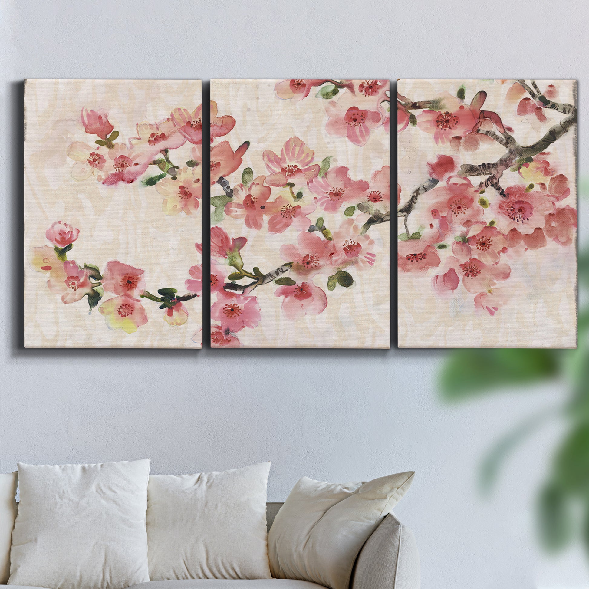Three-panel canvas wall art featuring blooming cherry blossom branches, displayed in a living room above a sofa.