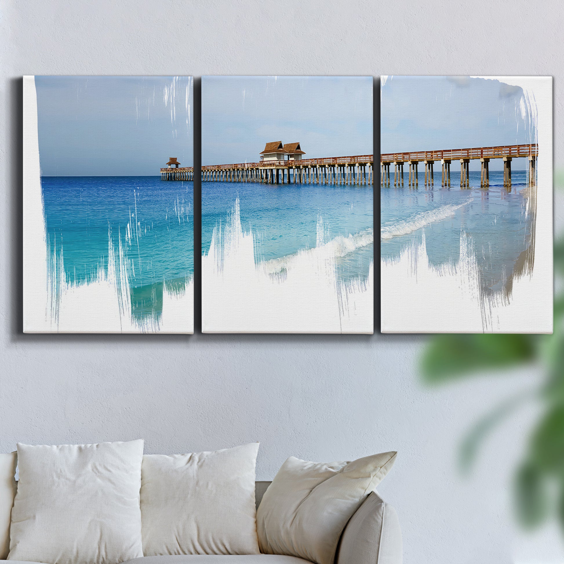 Three-panel canvas wall art featuring coastal pier extending over water, displayed in a living room above a sofa.