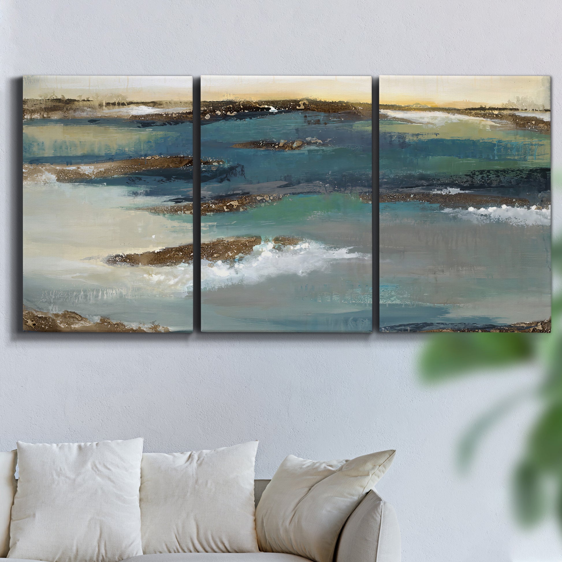 Three-panel canvas wall art featuring rocky coastal bluff above sea, displayed in a living room above a sofa.