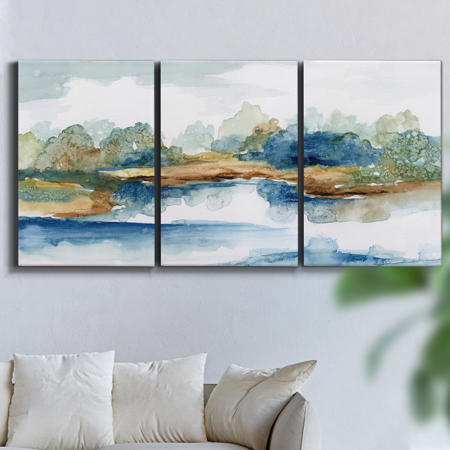 Three-panel canvas wall art featuring abstract blue watercolor landscape, displayed in a living room above a sofa.