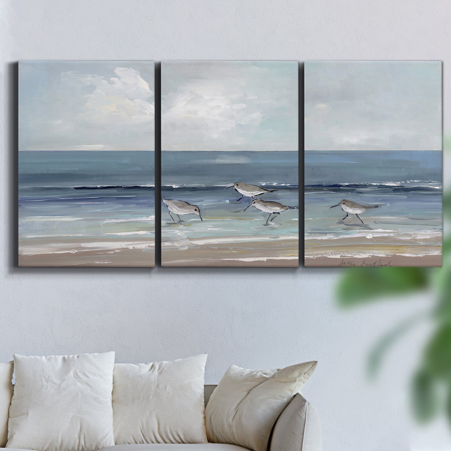 Three-panel canvas wall art featuring shore birds searching along beach, displayed in a living room above a sofa.