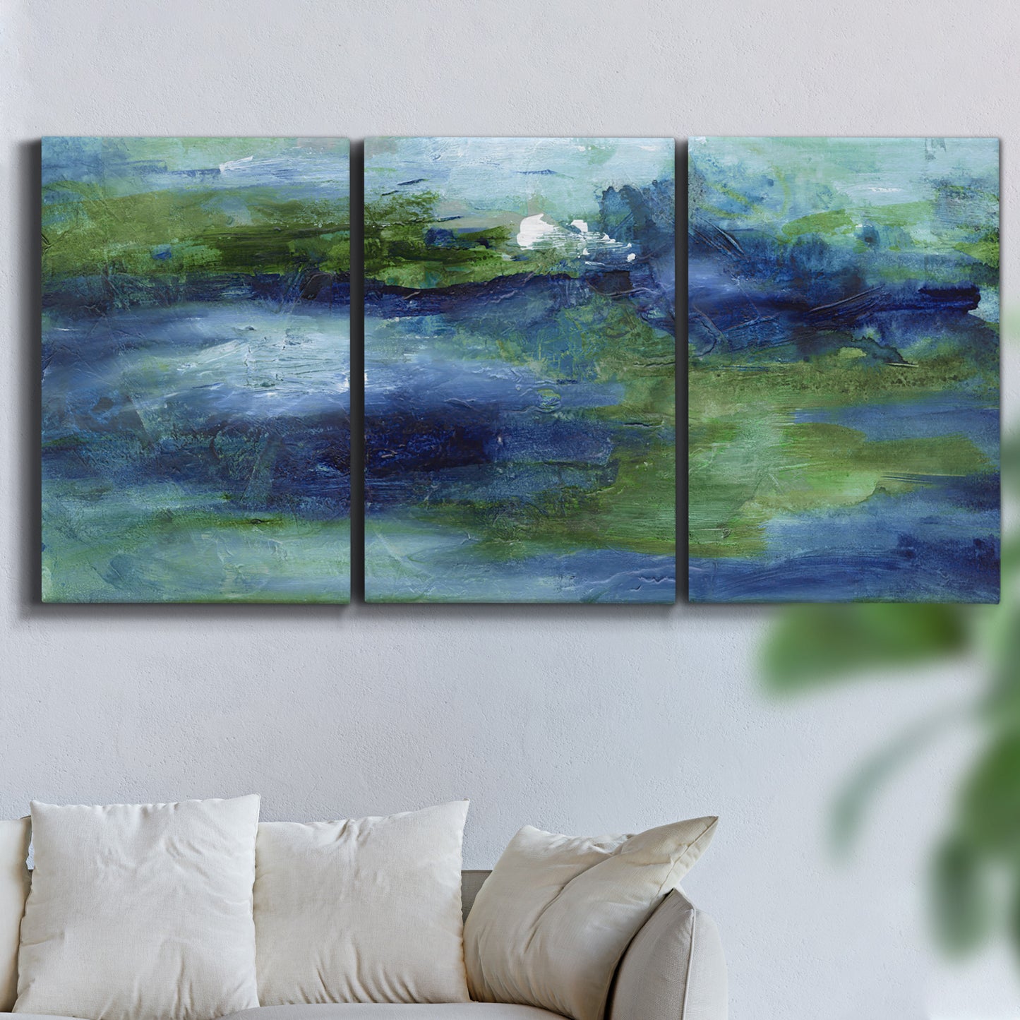 Three-panel canvas wall art featuring flowing blue abstract watercolor, displayed in a living room above a sofa.