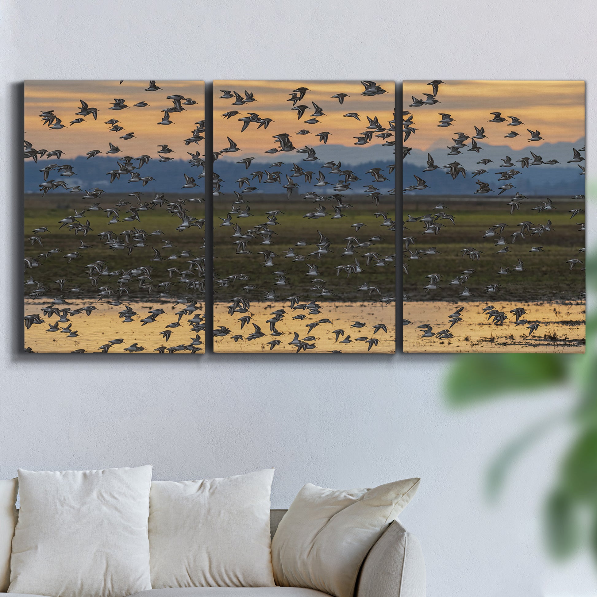 Three-panel canvas wall art featuring birds flying across sunset sky, displayed in a living room above a sofa.