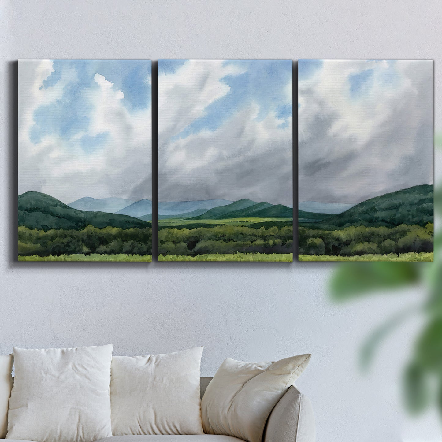 Three-panel canvas wall art featuring pastoral mountain landscape in blue, displayed in a living room above a sofa.