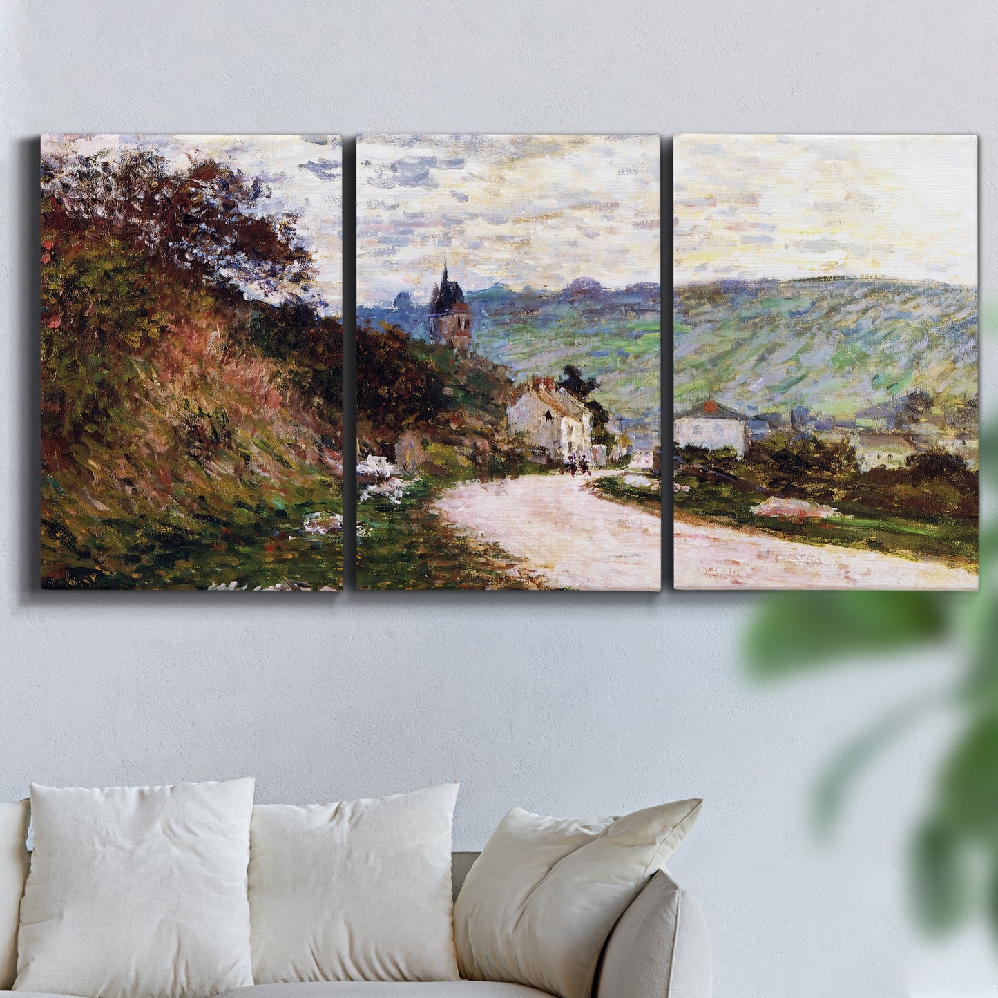 Three-panel canvas wall art featuring country road through village, displayed in a living room above a sofa.