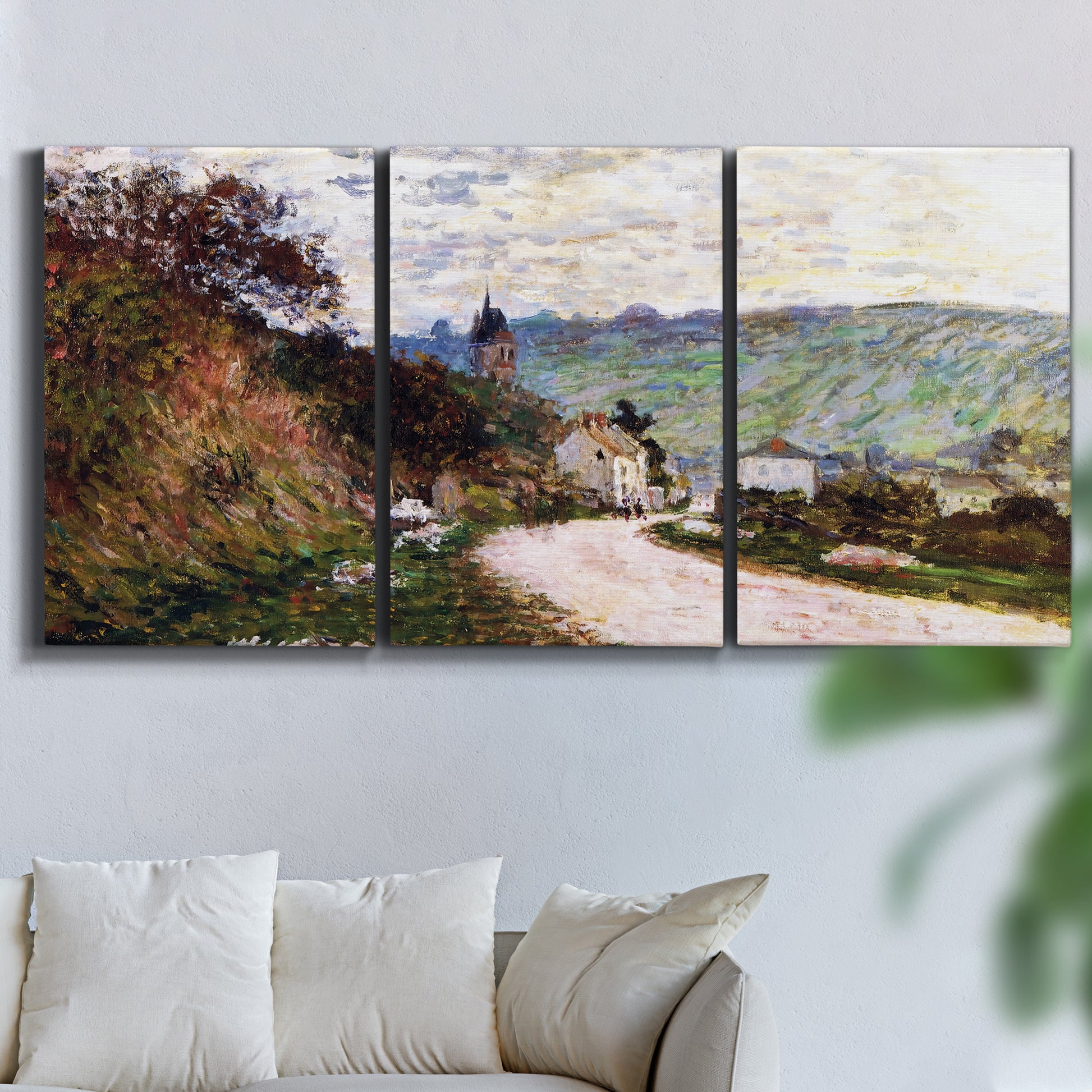 Three-panel canvas wall art featuring country road through village, displayed in a living room above a sofa.
