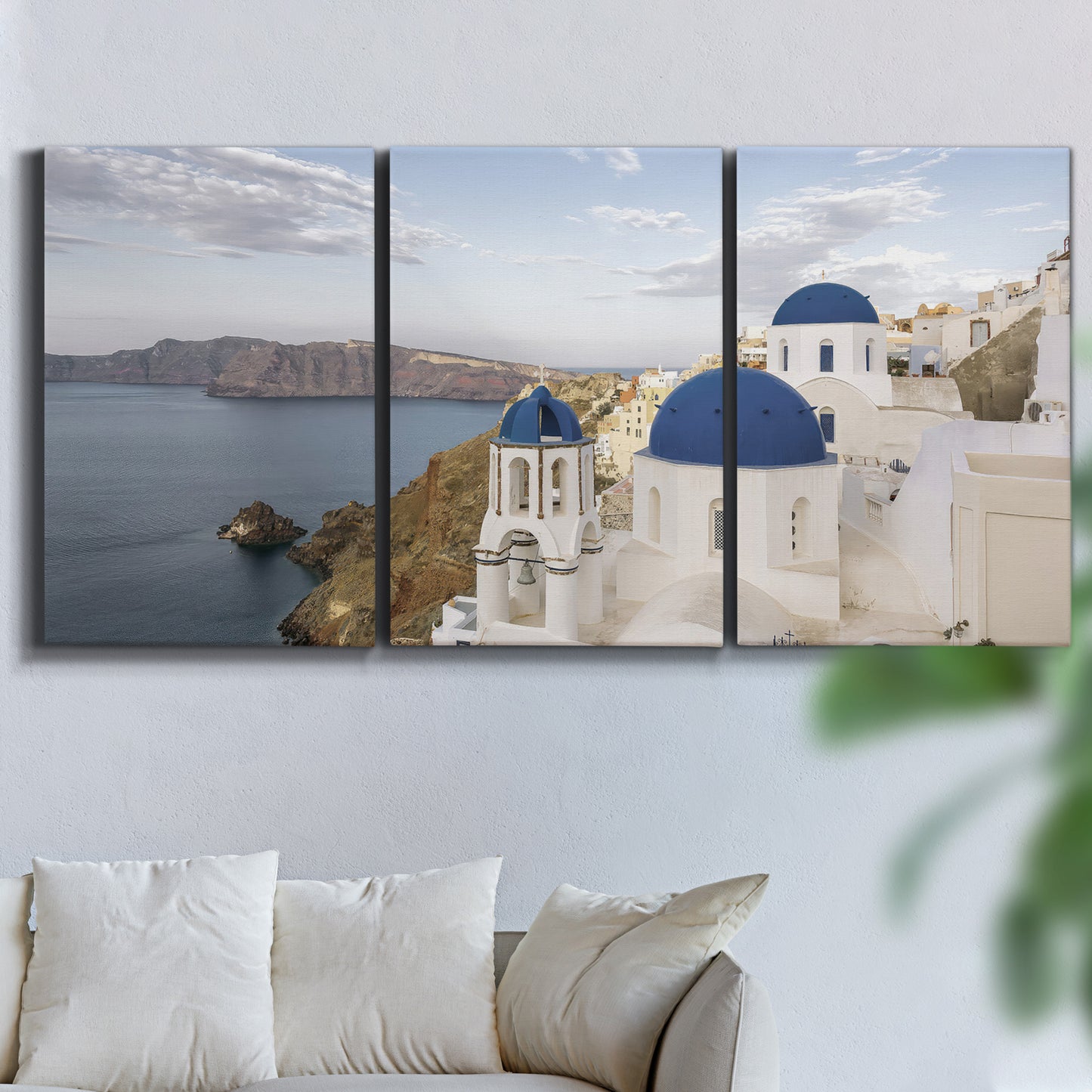 Three-panel canvas wall art featuring white buildings overlooking sea cliffs, displayed in a living room above a sofa.