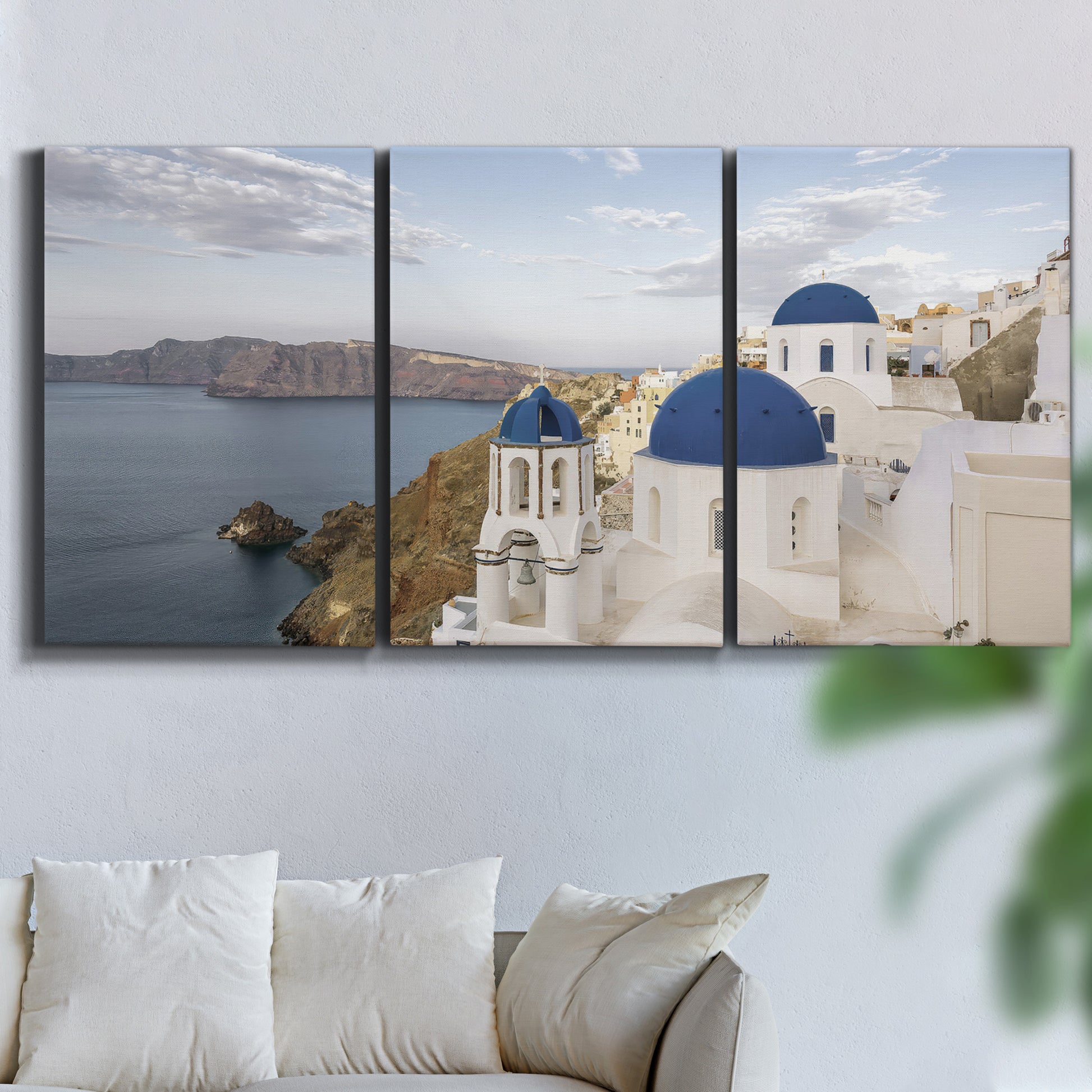 Three-panel canvas wall art featuring white buildings overlooking sea cliffs, displayed in a living room above a sofa.