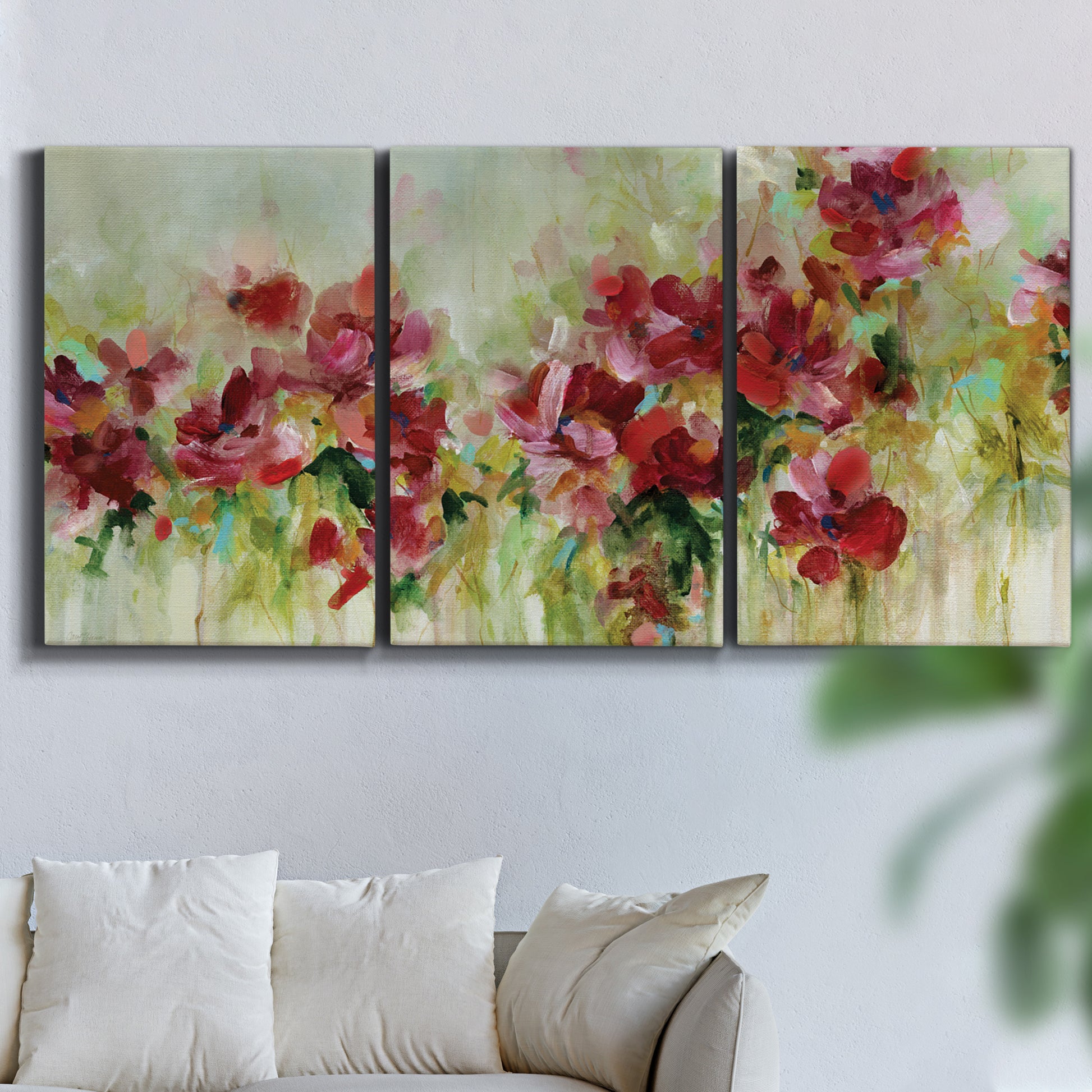 Three-panel canvas wall art featuring colorful floral garden composition, displayed in a living room above a sofa.