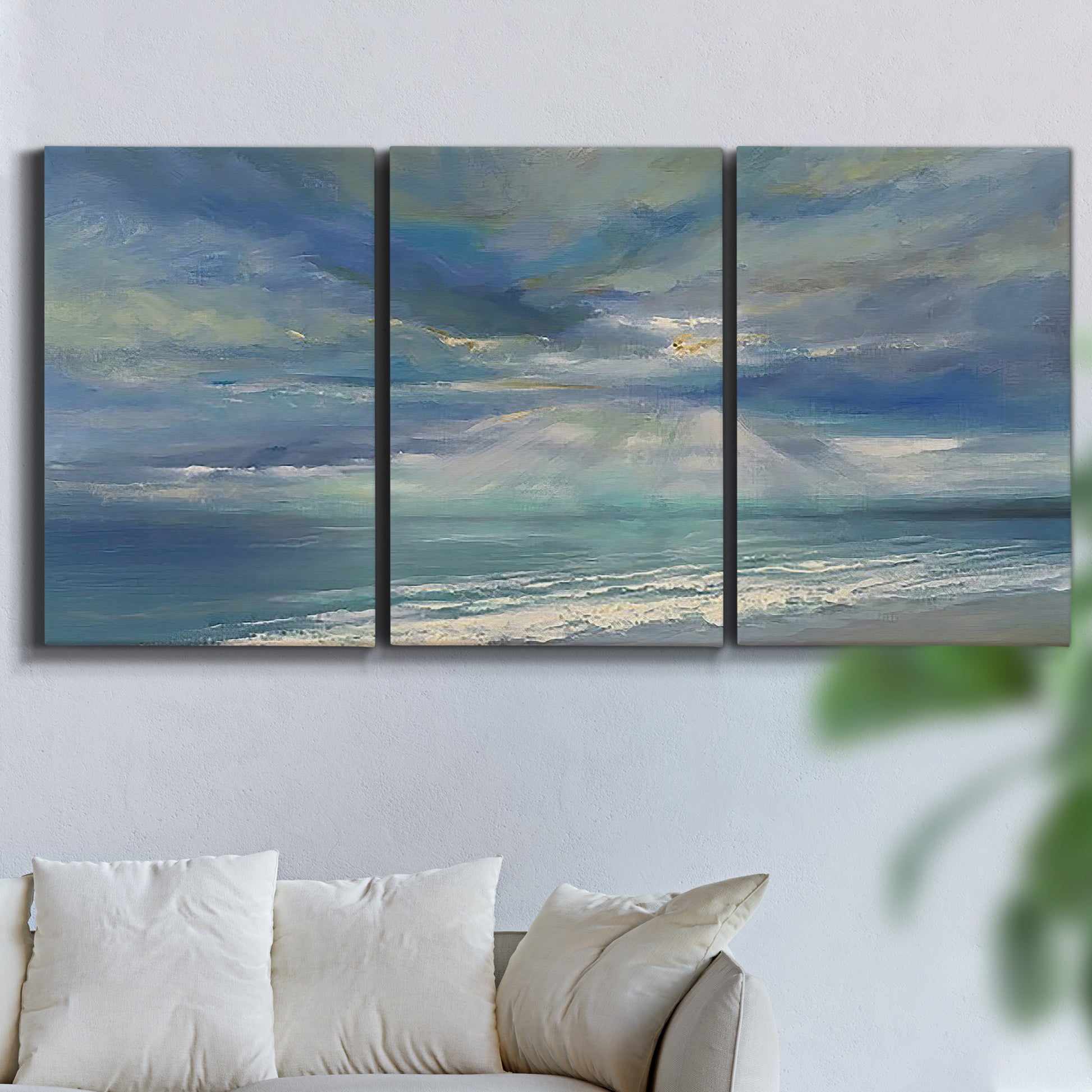 Three-panel canvas wall art featuring sunbeams breaking through coastal clouds, displayed in a living room above a sofa.