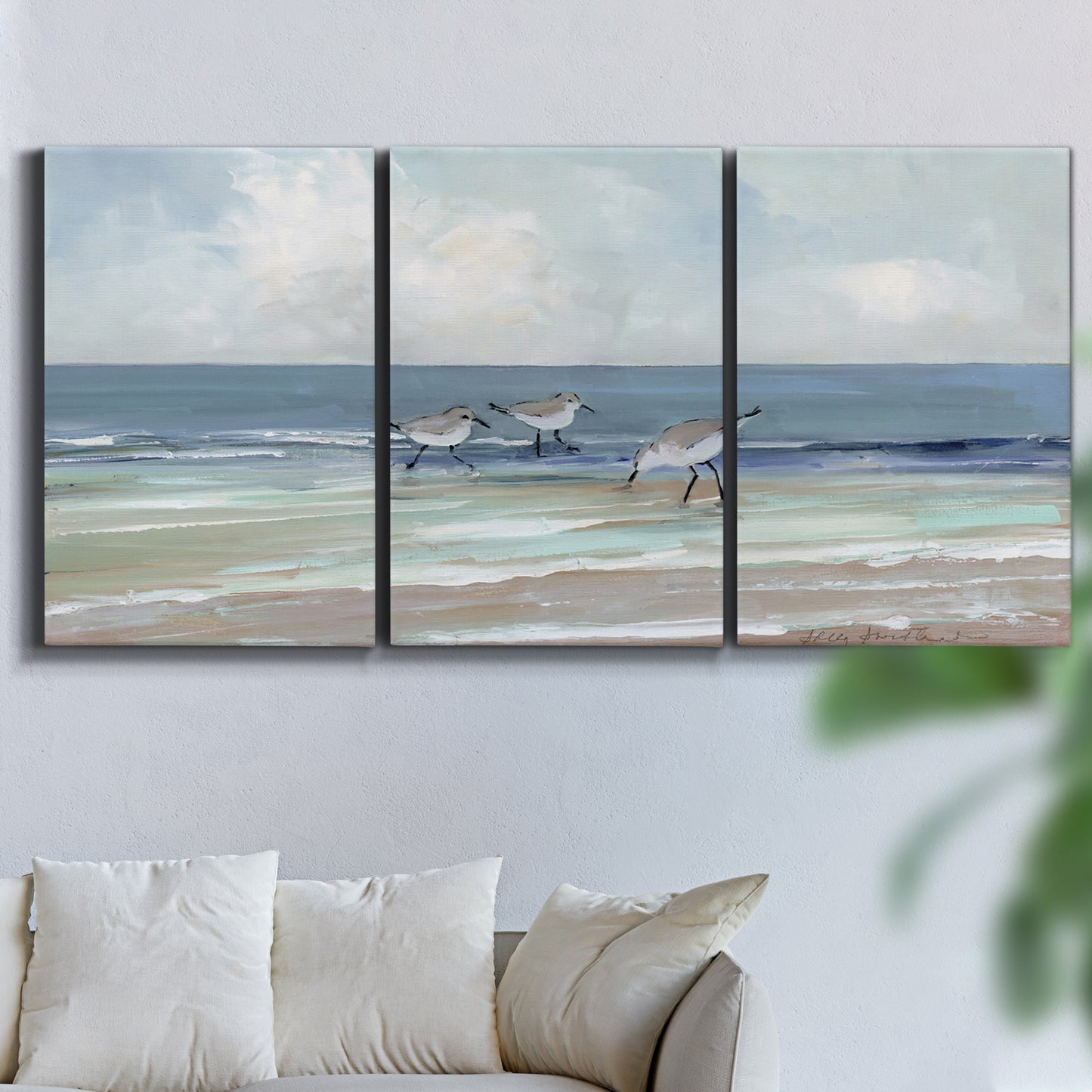 Three-panel canvas wall art featuring shore birds searching along beach, displayed in a living room above a sofa.