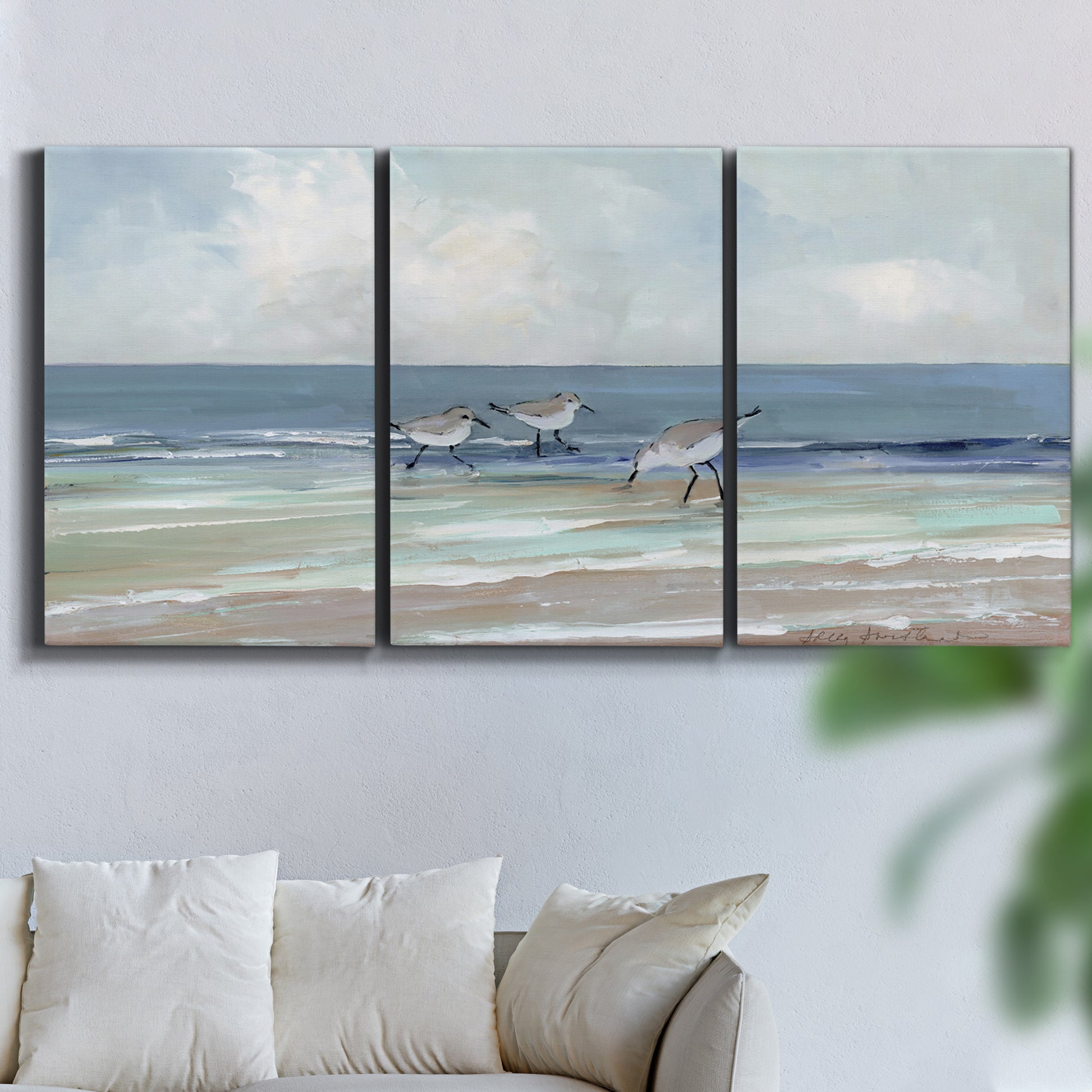 Three-panel canvas wall art featuring shore birds searching along beach, displayed in a living room above a sofa.