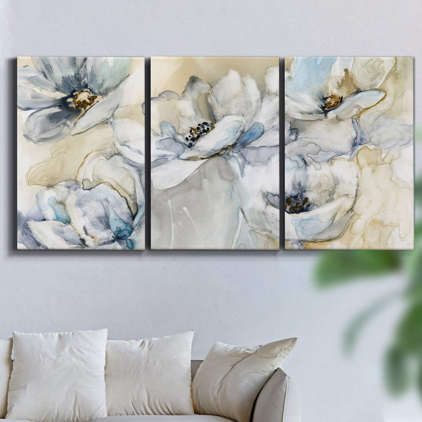Three-panel canvas wall art featuring delicate watercolor floral blooms, displayed in a living room above a sofa.