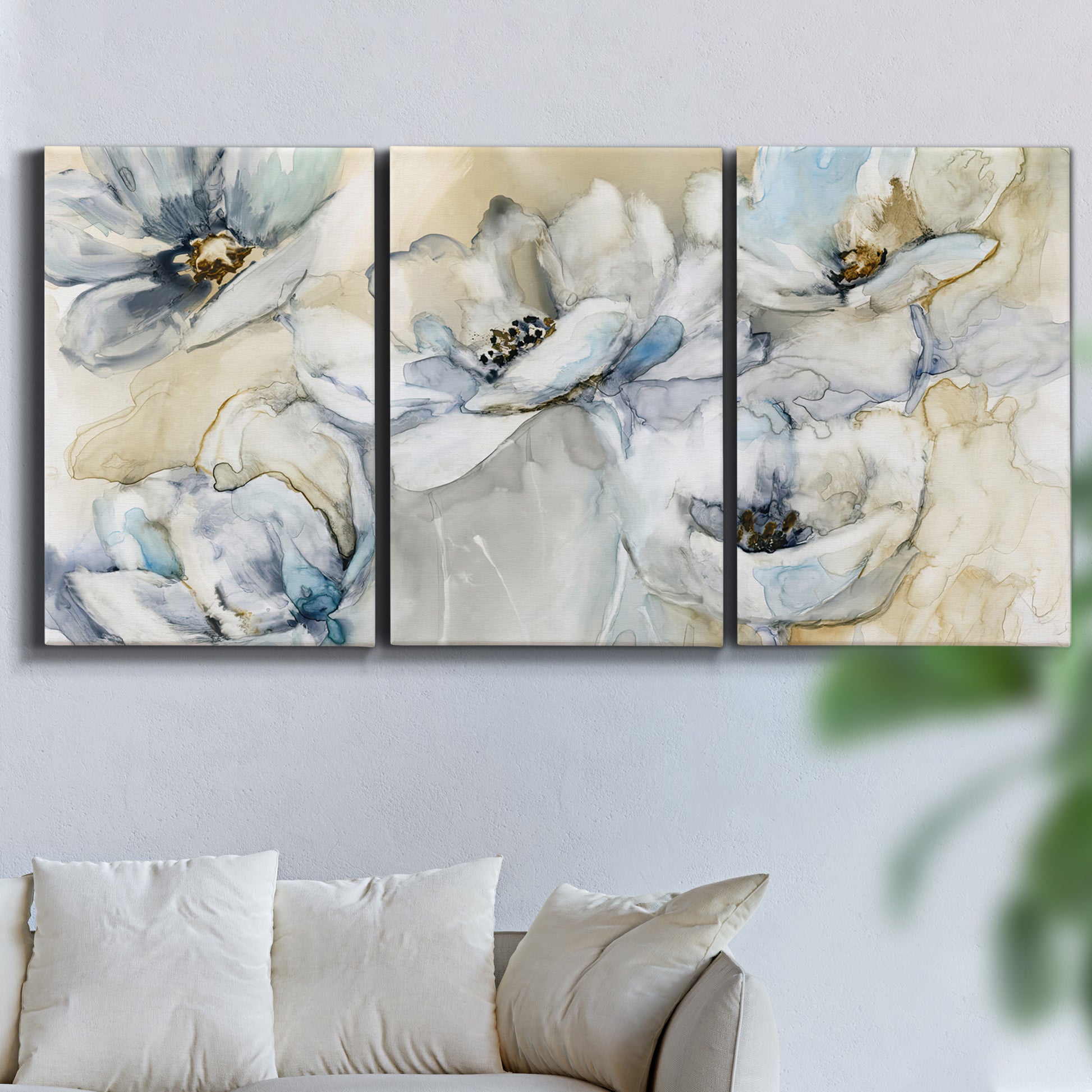 Three-panel canvas wall art featuring delicate watercolor floral blooms, displayed in a living room above a sofa.