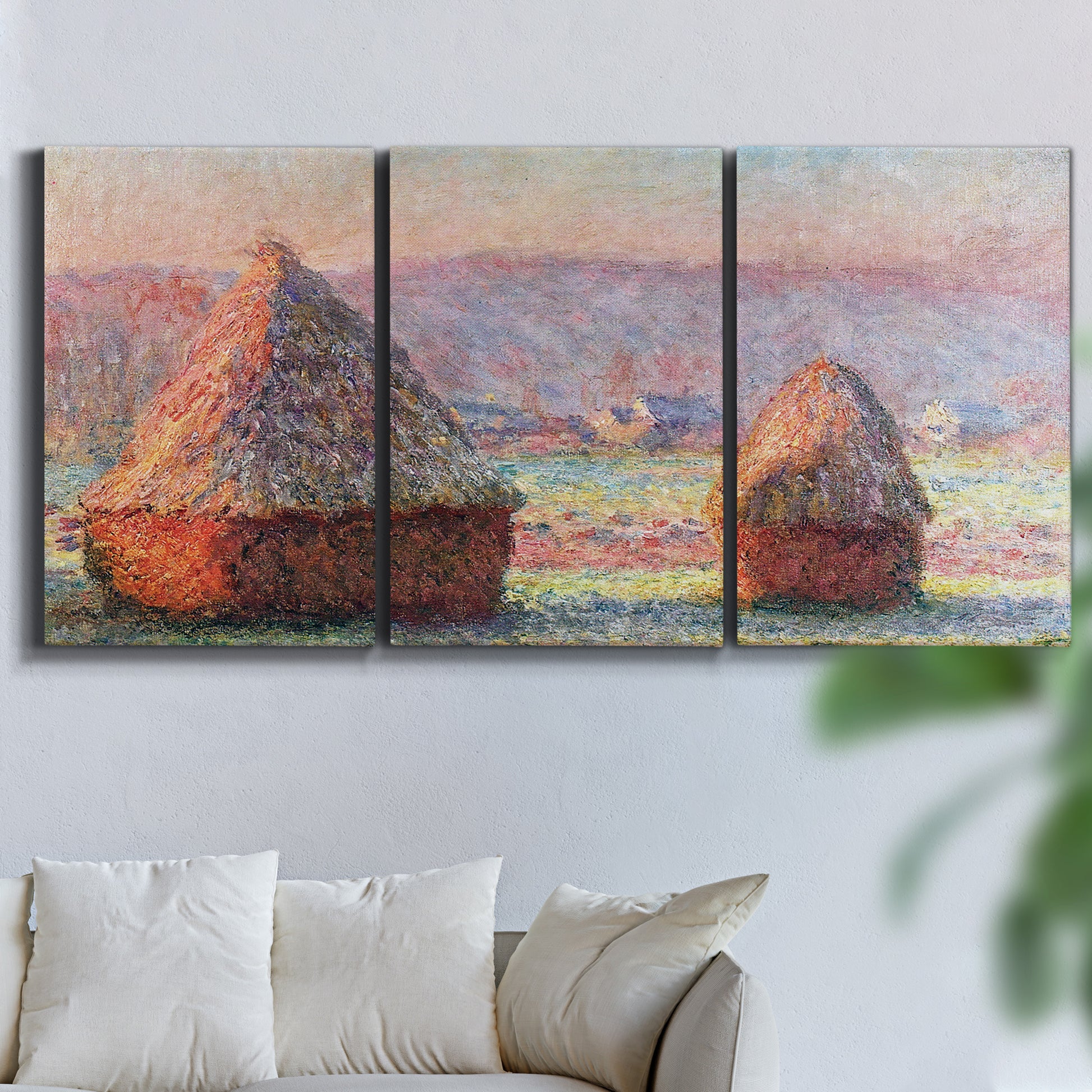 Three-panel canvas wall art featuring winter grainstacks glowing at sunset, displayed in a living room above a sofa.