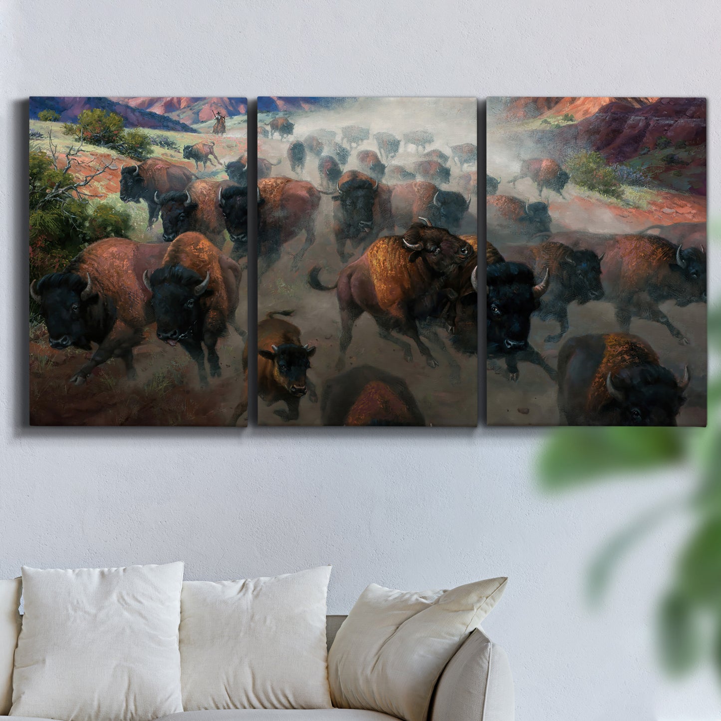 Three-panel canvas wall art featuring stormy canyon landscape with animals, displayed in a living room above a sofa.