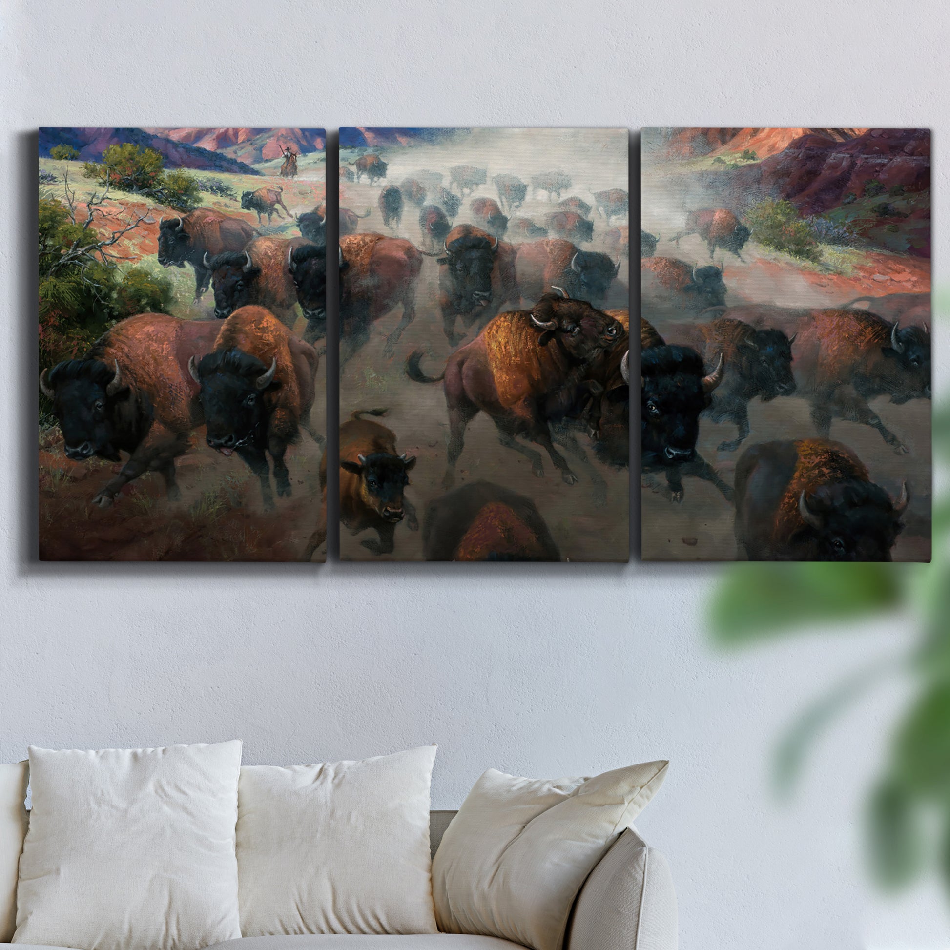 Three-panel canvas wall art featuring stormy canyon landscape with animals, displayed in a living room above a sofa.