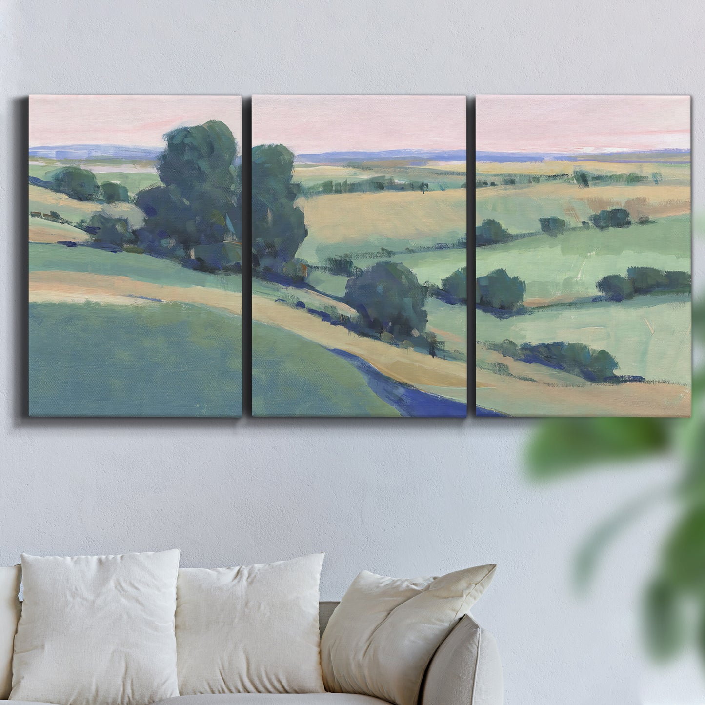 Three-panel canvas wall art featuring pastoral countryside with rocky outcrop, displayed in a living room above a sofa.