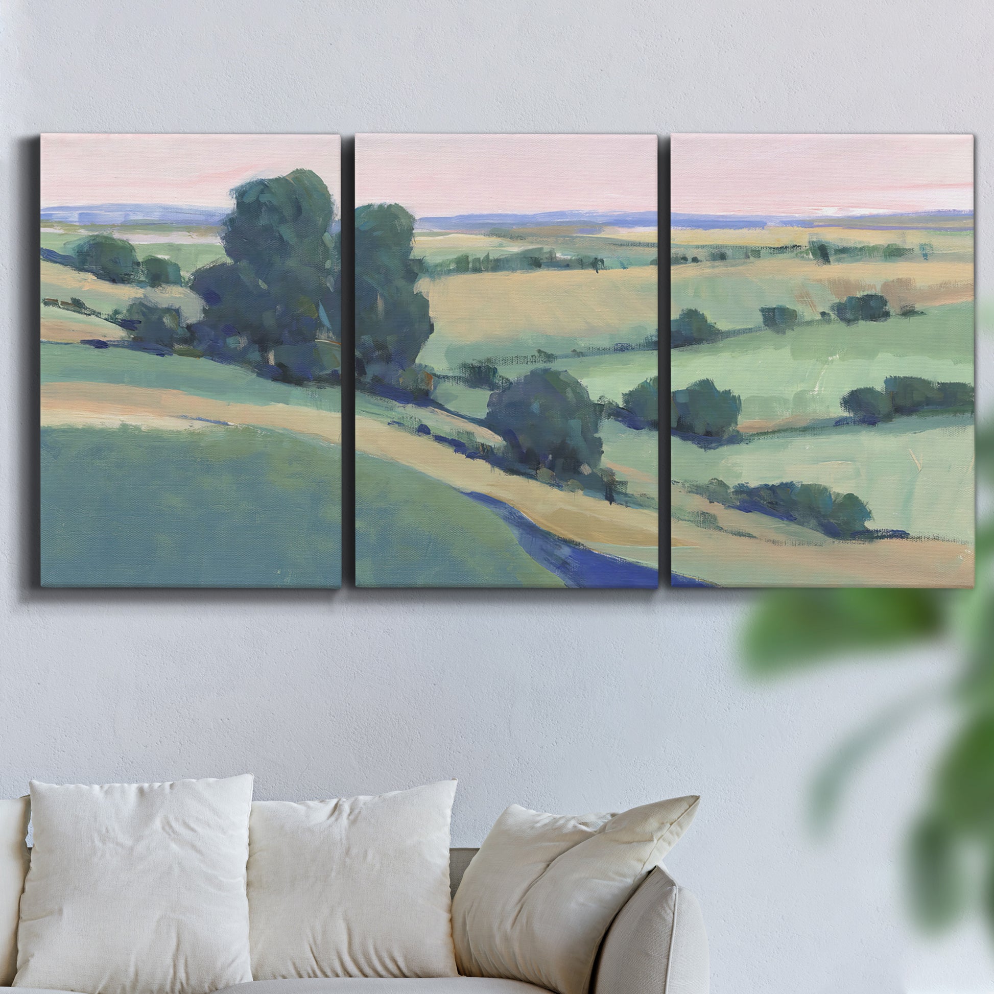 Three-panel canvas wall art featuring pastoral countryside with rocky outcrop, displayed in a living room above a sofa.