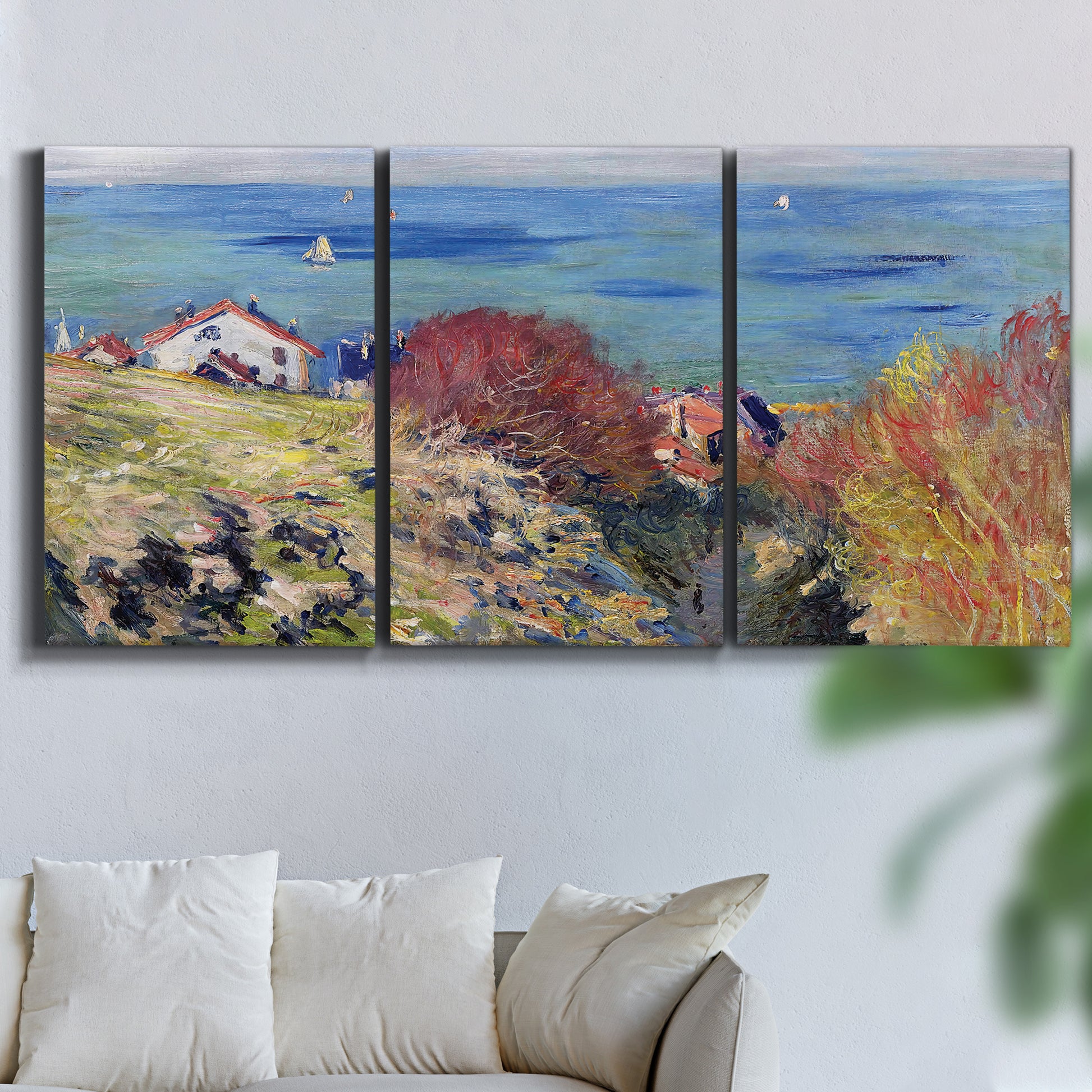 Three-panel canvas wall art featuring coastal village shoreline landscape, displayed in a living room above a sofa.