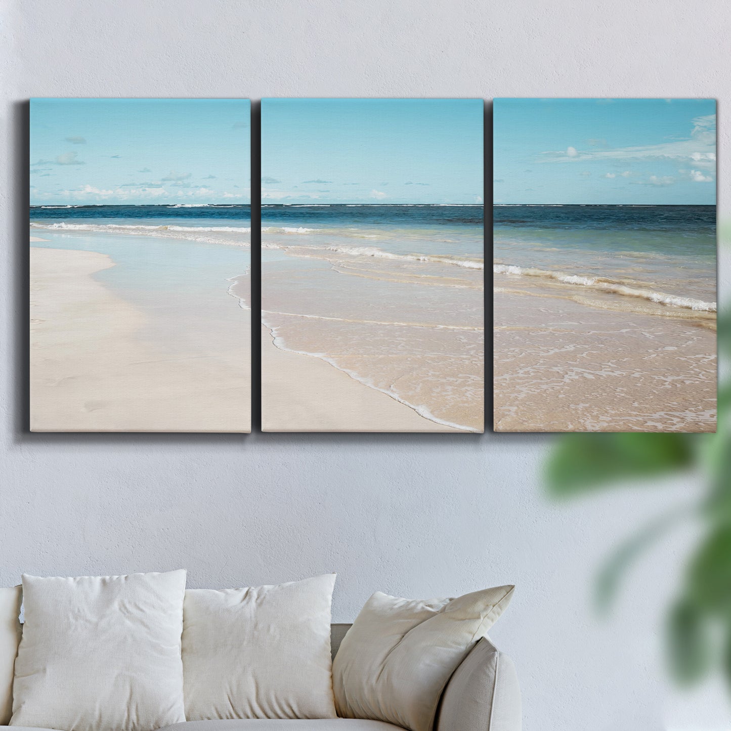 Three-panel canvas wall art featuring white sand beach with gentle waves, displayed in a living room above a sofa.