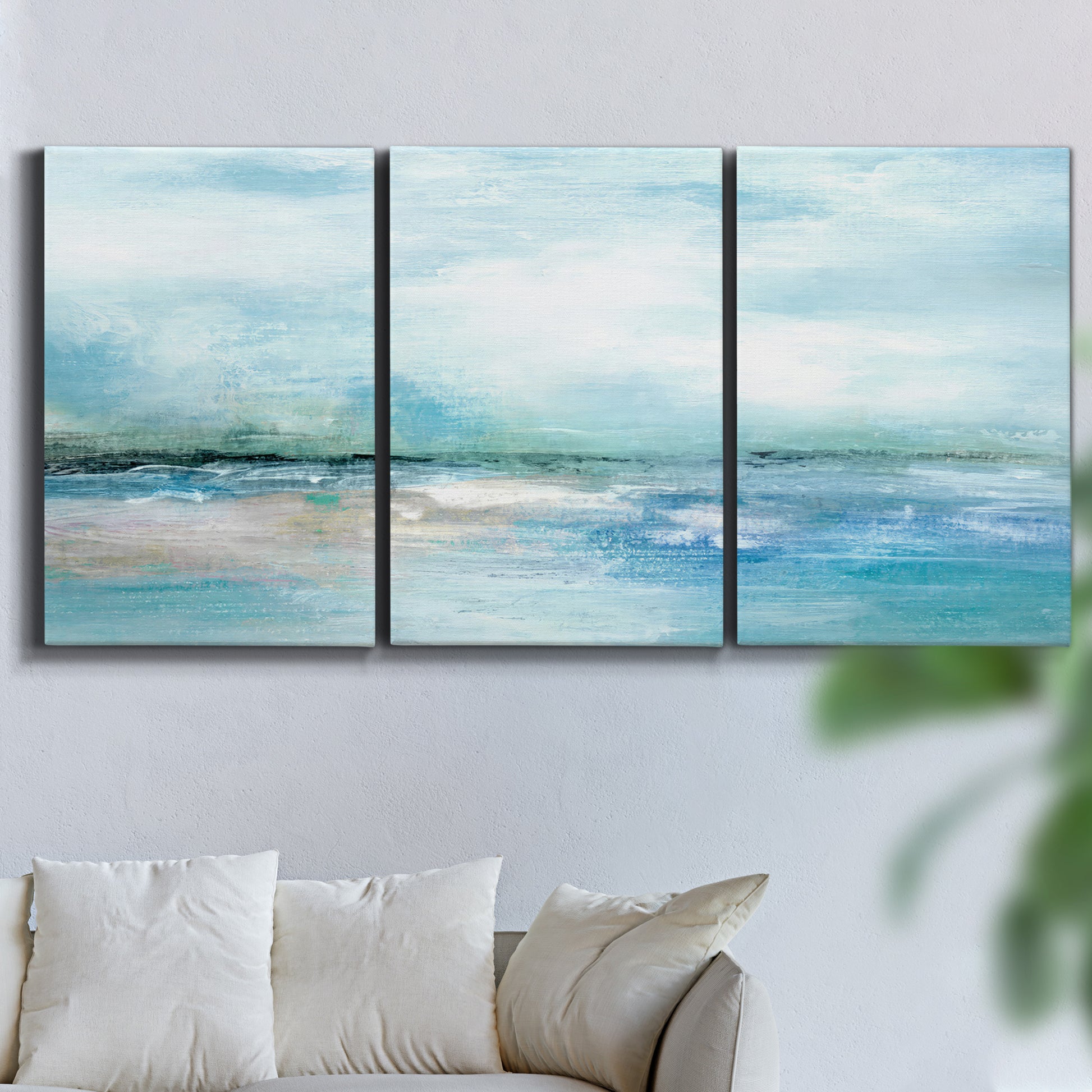 Three-panel canvas wall art featuring sunset silhouette over coastal water, displayed in a living room above a sofa.