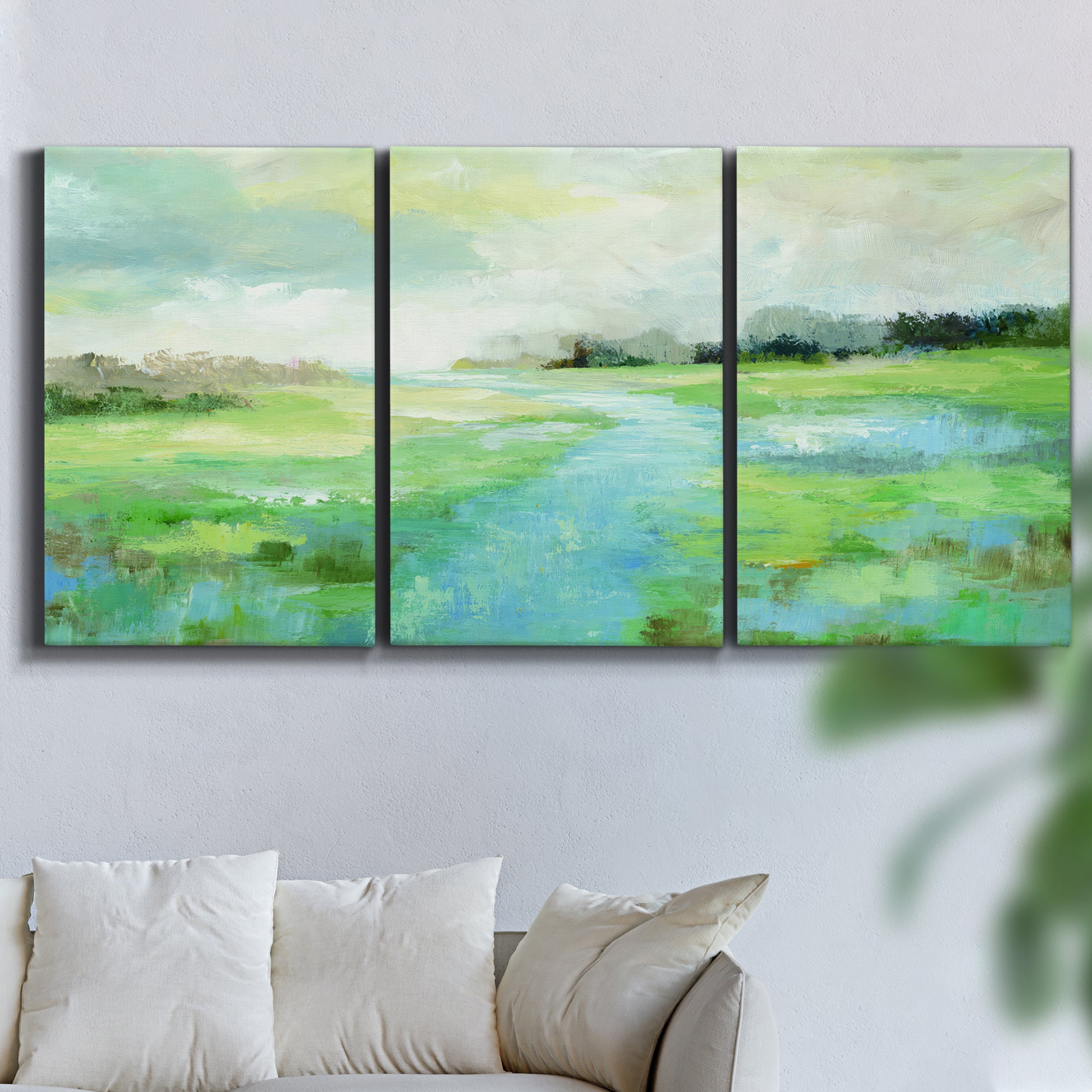 Three-panel canvas wall art featuring gentle stream winding through trees, displayed in a living room above a sofa.