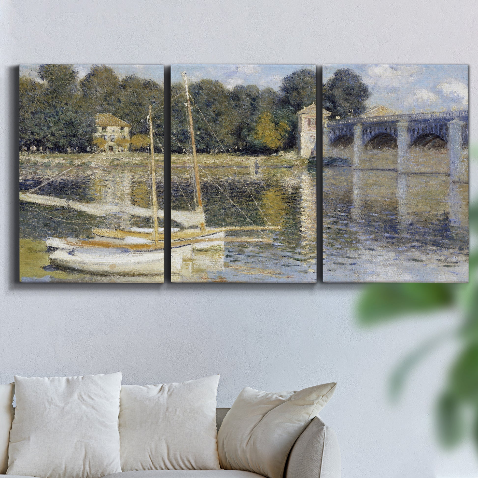 Three-panel canvas wall art featuring bridge crossing broad river, displayed in a living room above a sofa.