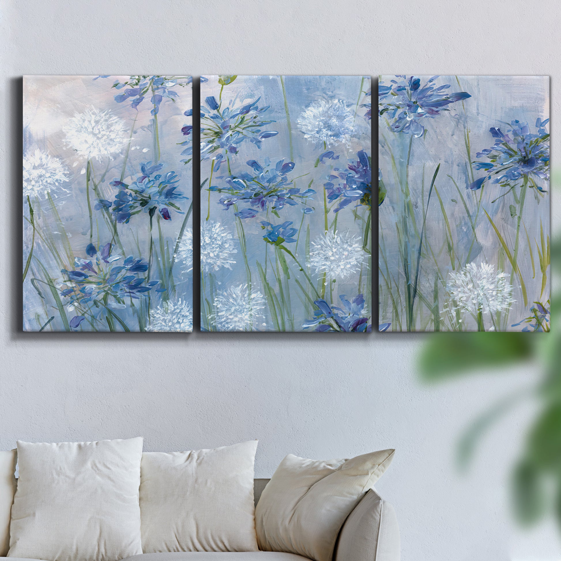 Three-panel canvas wall art featuring delicate watercolor floral blooms, displayed in a living room above a sofa.
