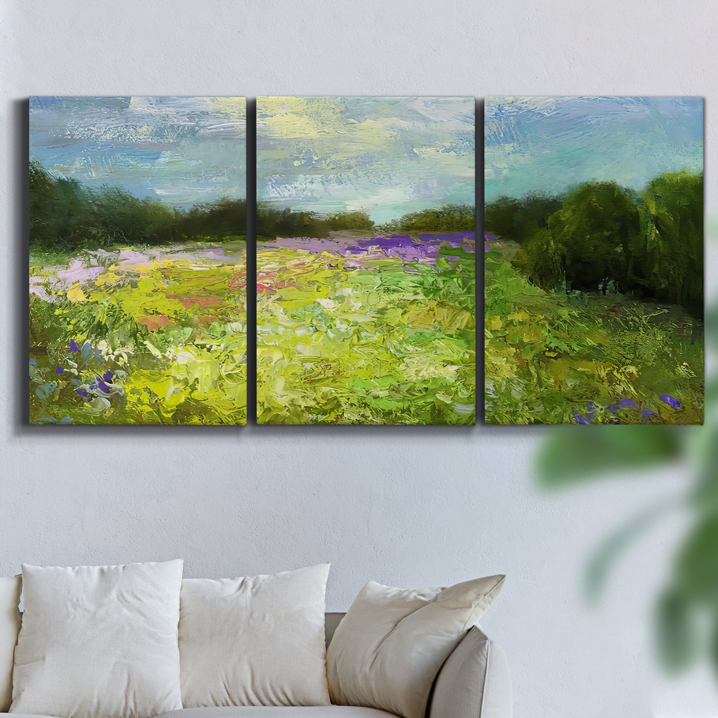 Three-panel canvas wall art featuring pastoral field with wildflowers, displayed in a living room above a sofa.