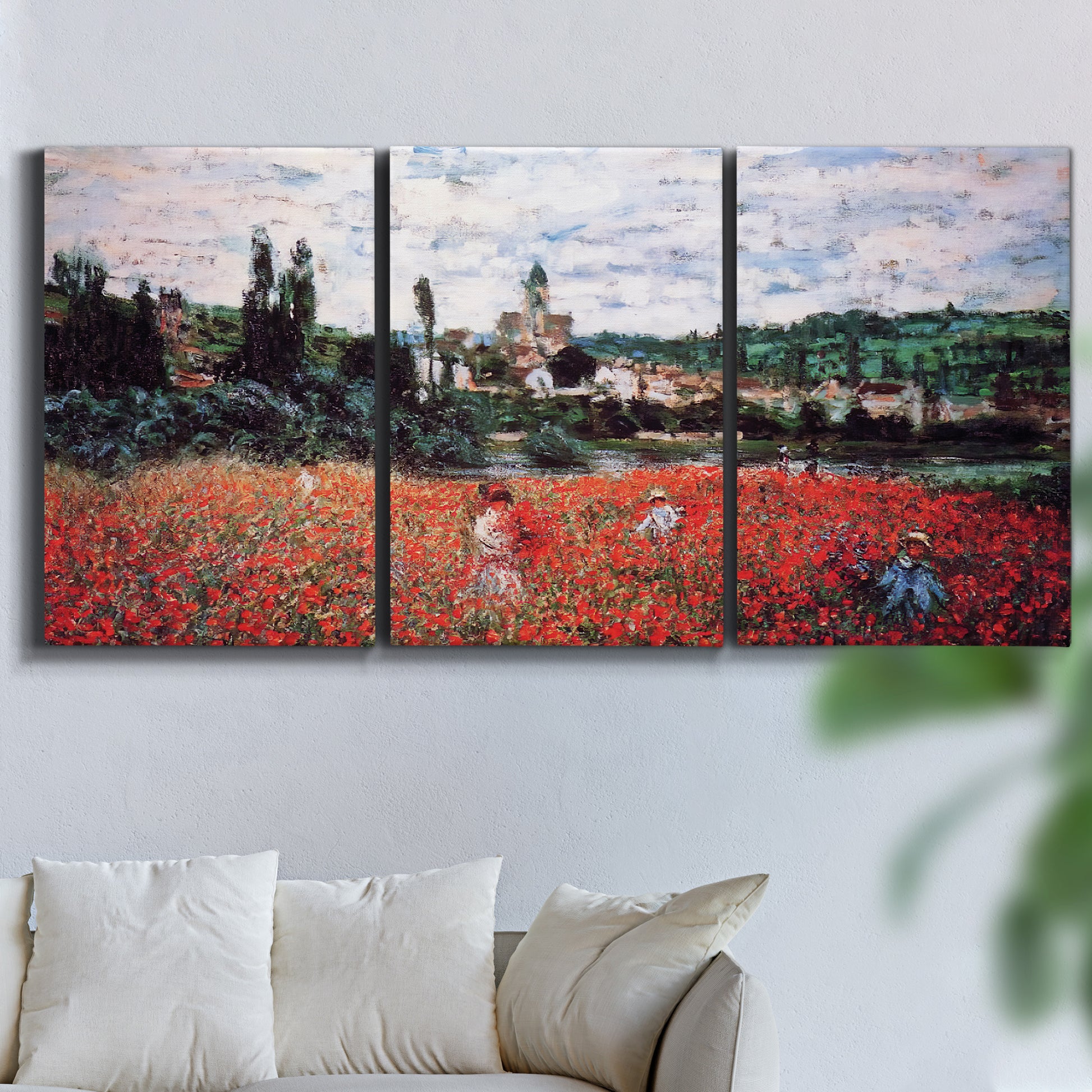 Three-panel canvas wall art featuring poppy field beside village landscape, displayed in a living room above a sofa.