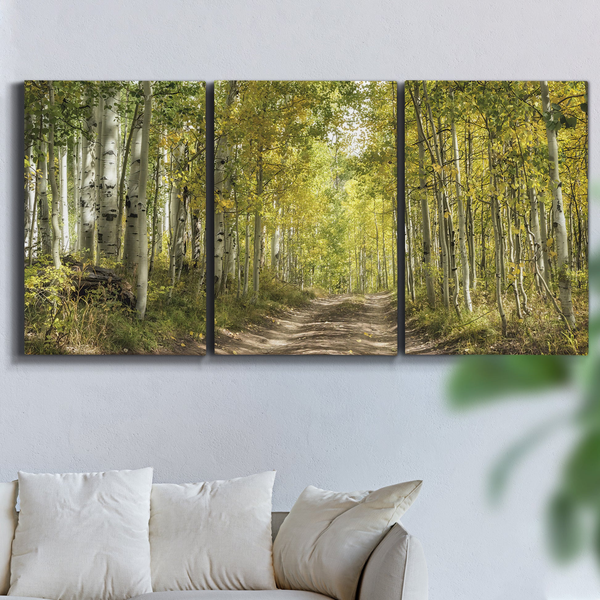 Three-panel canvas wall art featuring tree lined forest road photograph, displayed in a living room above a sofa.