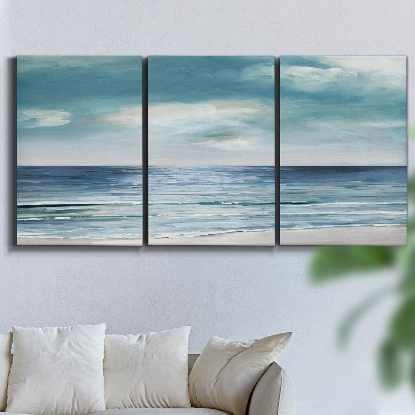 Three-panel canvas wall art featuring calm coastal shoreline, displayed in a living room above a sofa.