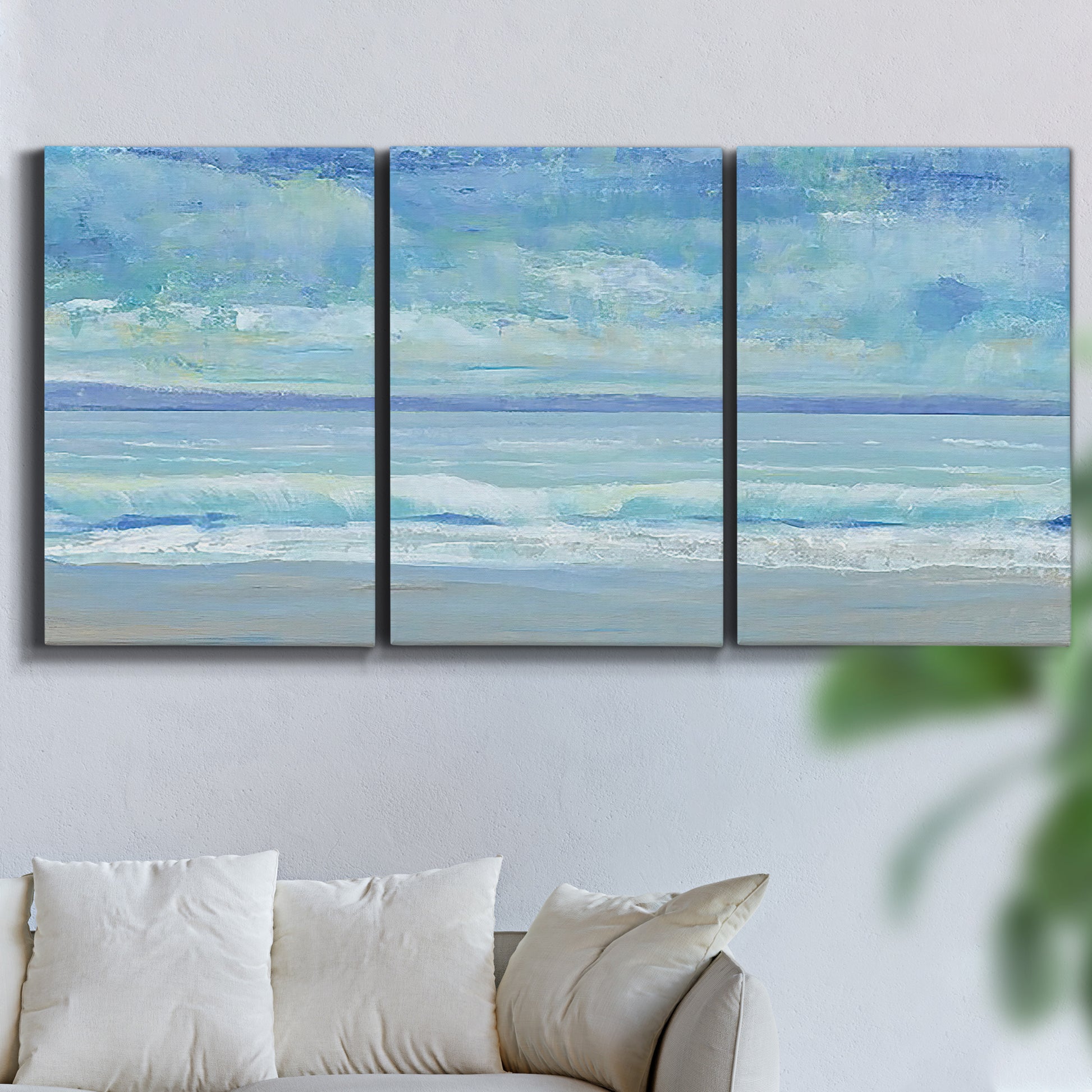 Three-panel canvas wall art featuring rolling ocean surf along shoreline, displayed in a living room above a sofa.